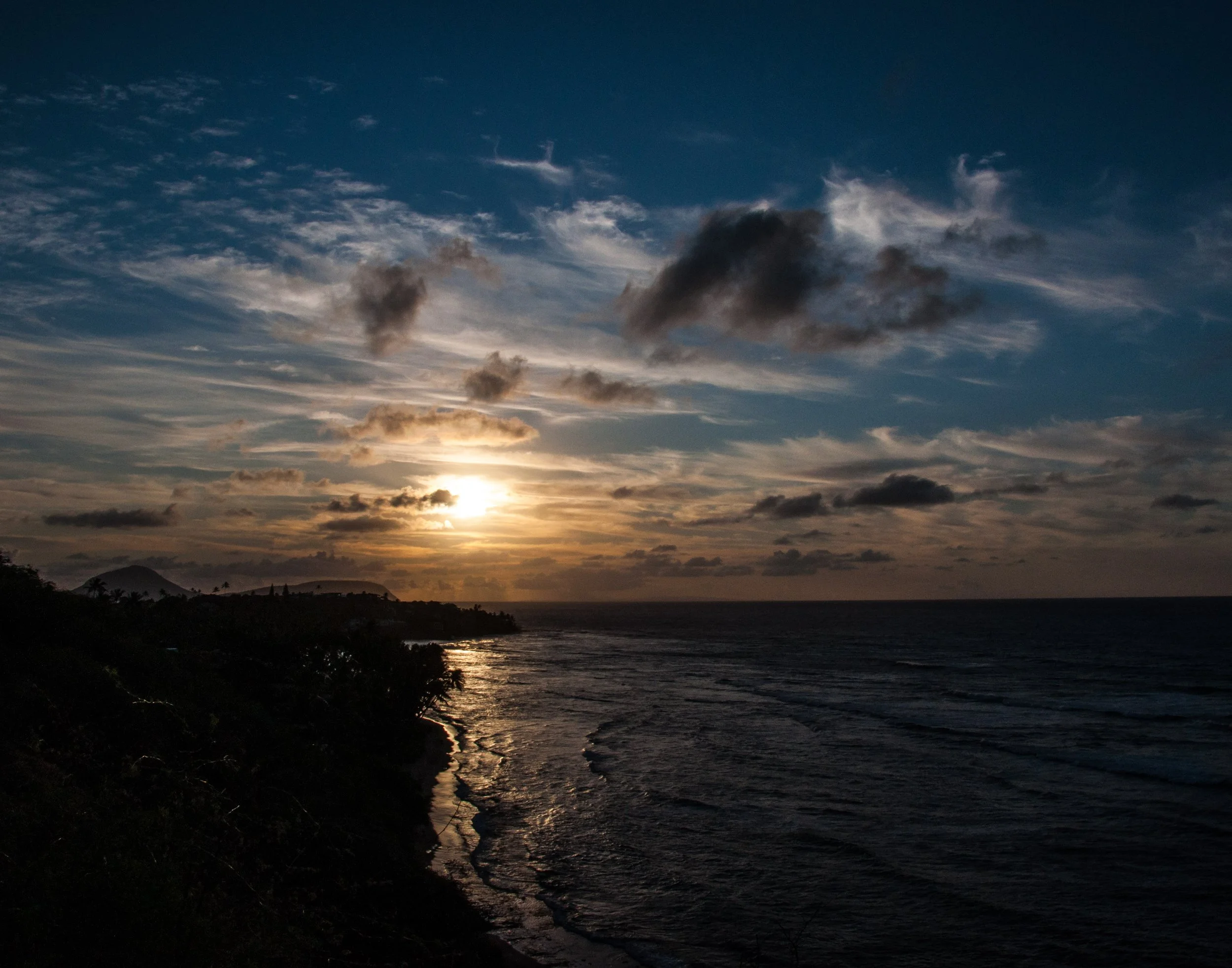 Sunset over a beach with waves and scattered clouds in the sky.