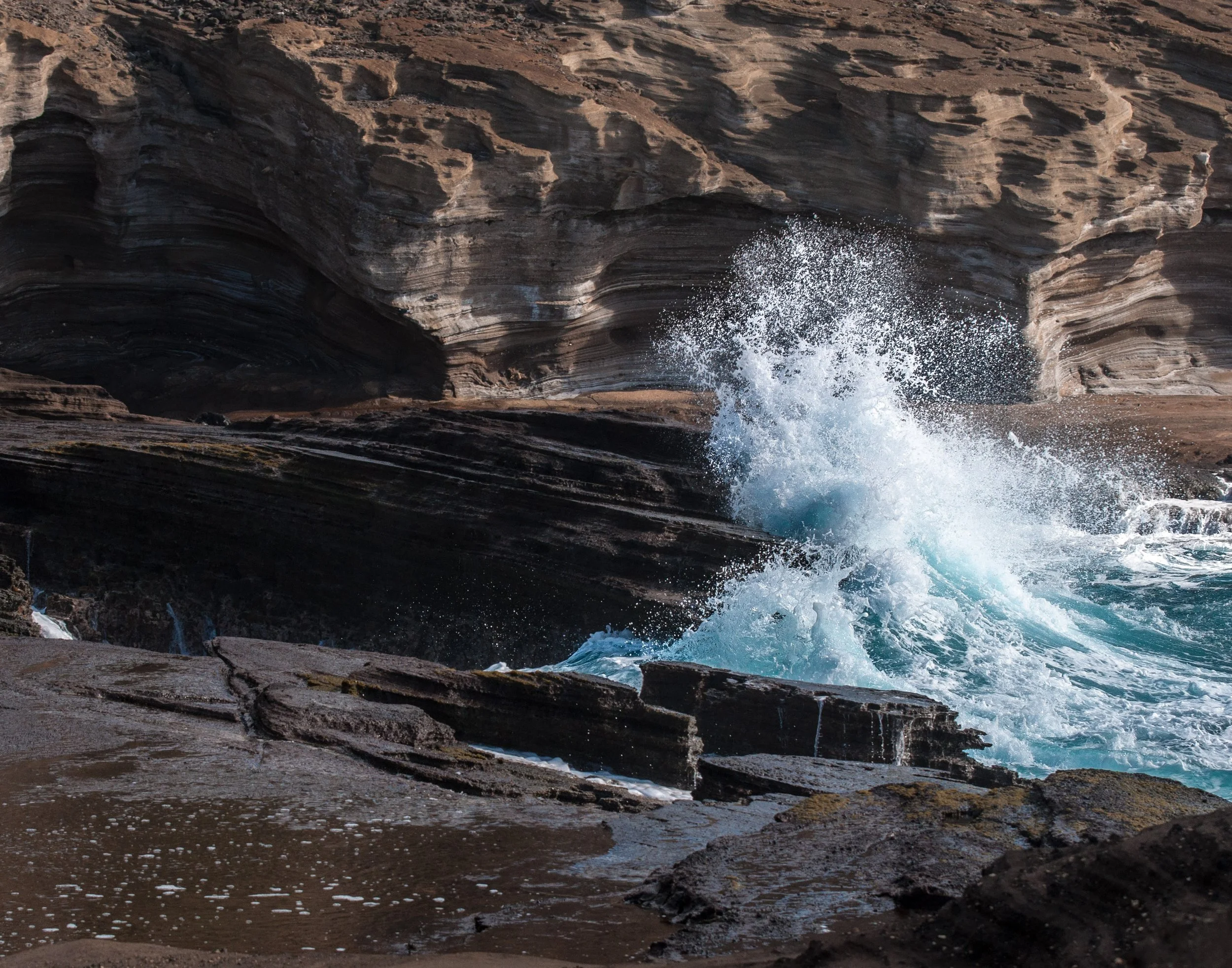 Waves crashing against rocky shore with layered cliffs in background.