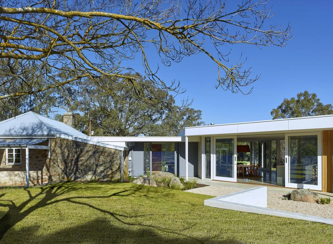 Modern house with large windows, surrounded by a well-kept lawn and trees with some bare branches, under a clear blue sky.