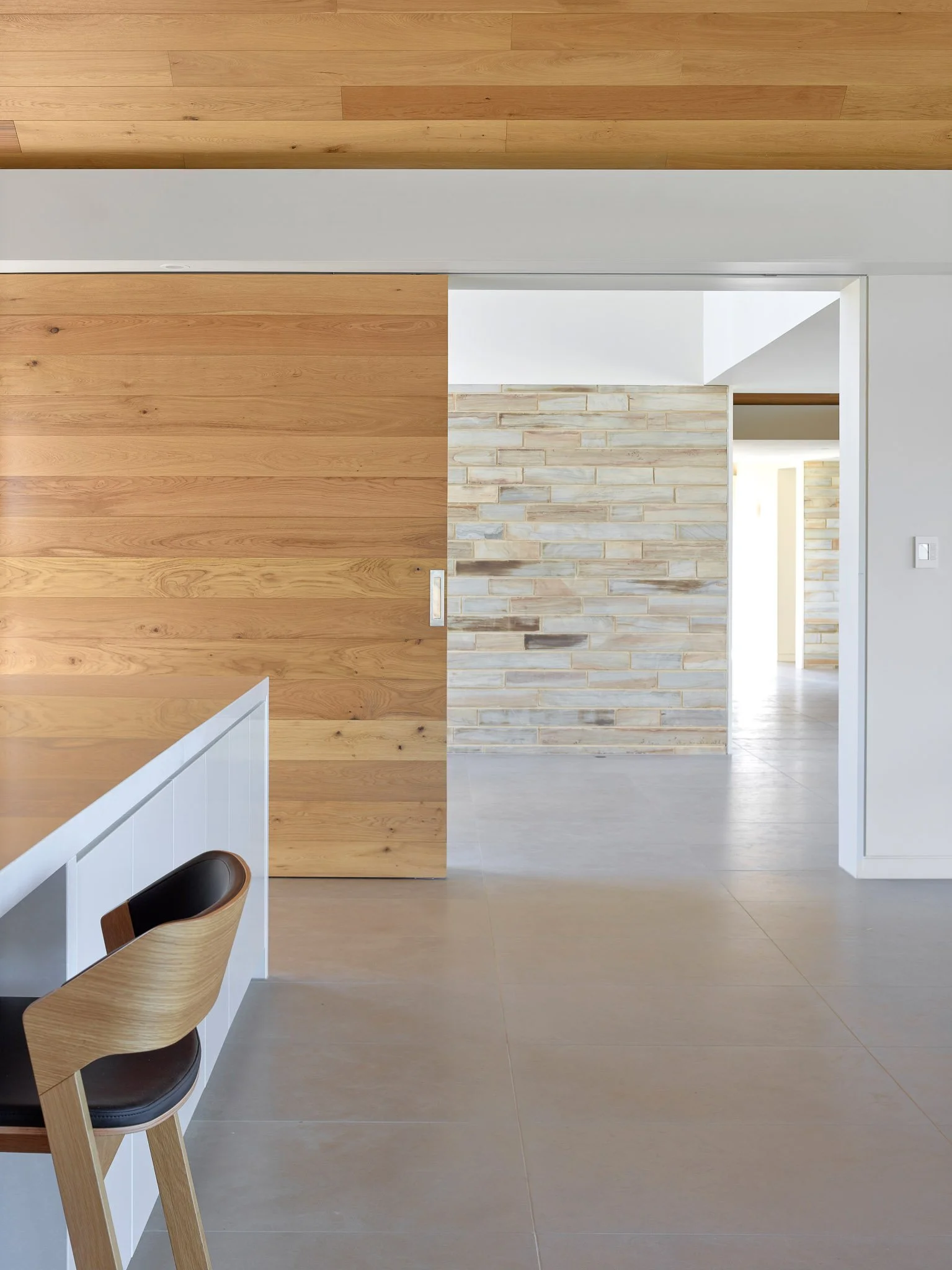 Modern interior with wooden sliding door, brick wall, and minimalistic furniture in neutral colors.