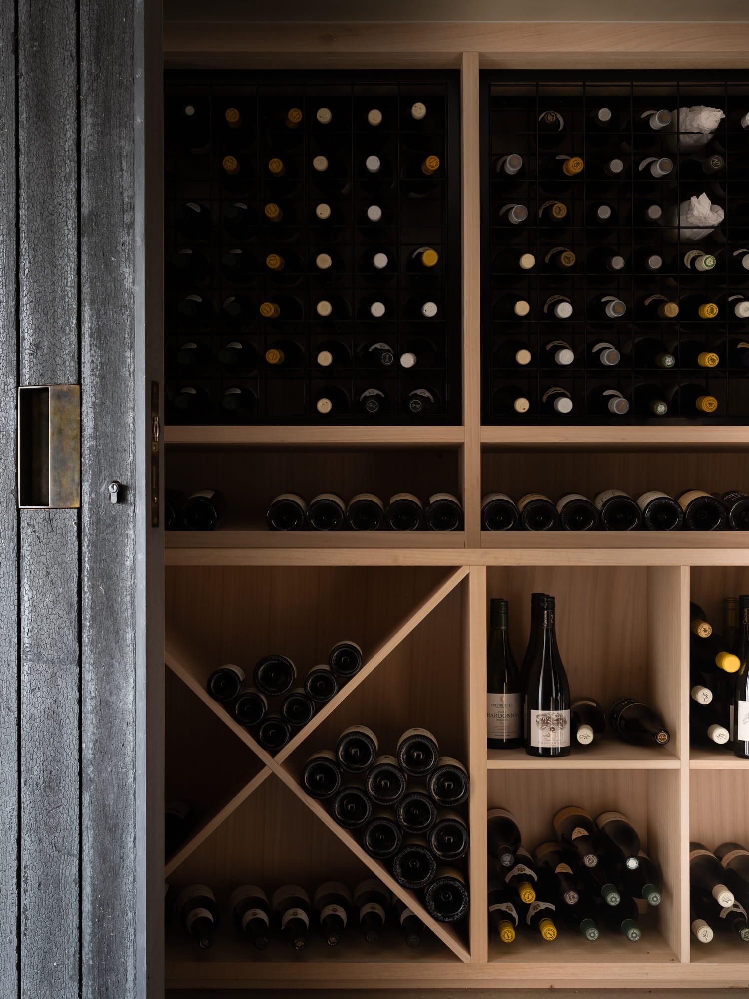 Wooden wine rack filled with various bottles of wine, some with crumpled paper inserts, next to a rustic, weathered door.
