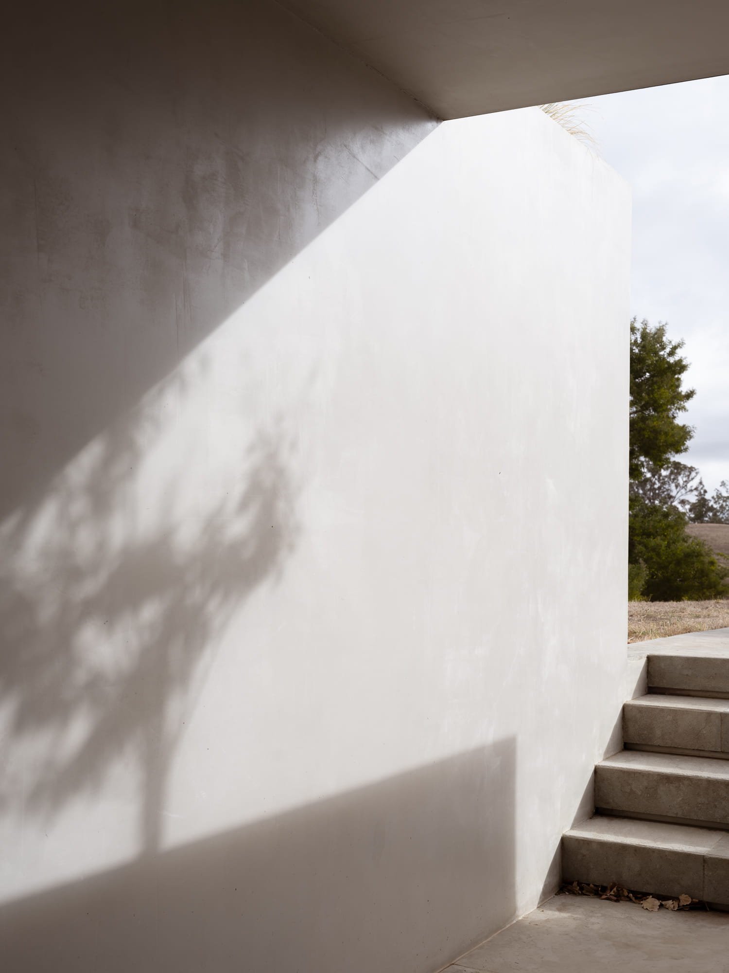 An outdoor concrete staircase with a white wall and exterior landscape visible in the background.
