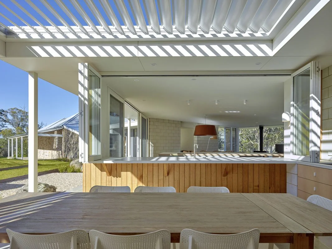 Open-concept dining and living area with large windows, natural sunlight, and modern minimalist design.