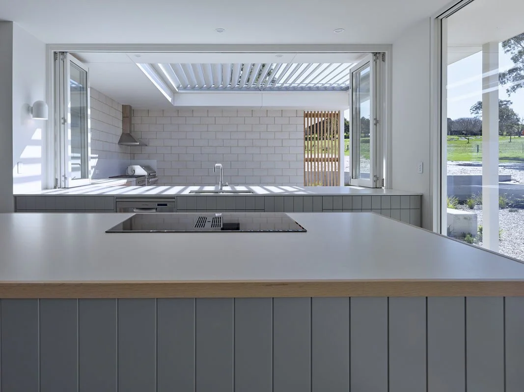 Modern kitchen with large open windows, white countertop, electric cooktop, and view of outdoor patio and green landscape.