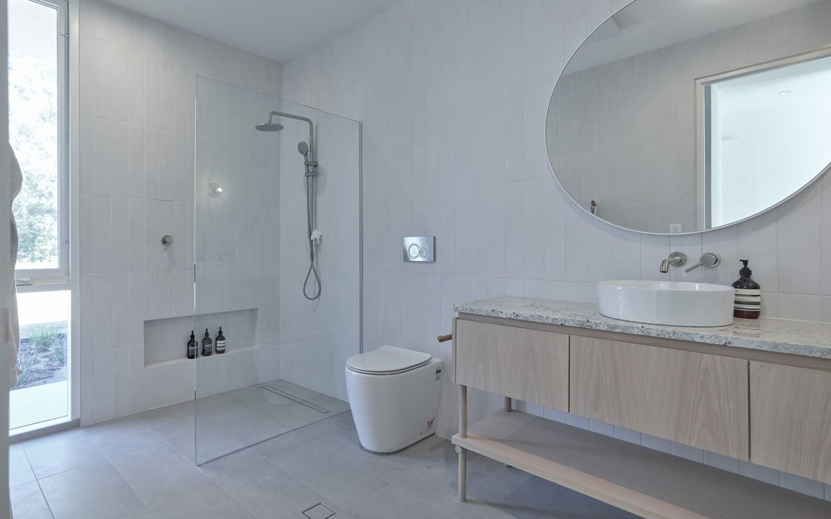 Modern bathroom with a walk-in shower, a white toilet, a wooden vanity with a granite countertop, a vessel sink, and a large oval mirror.