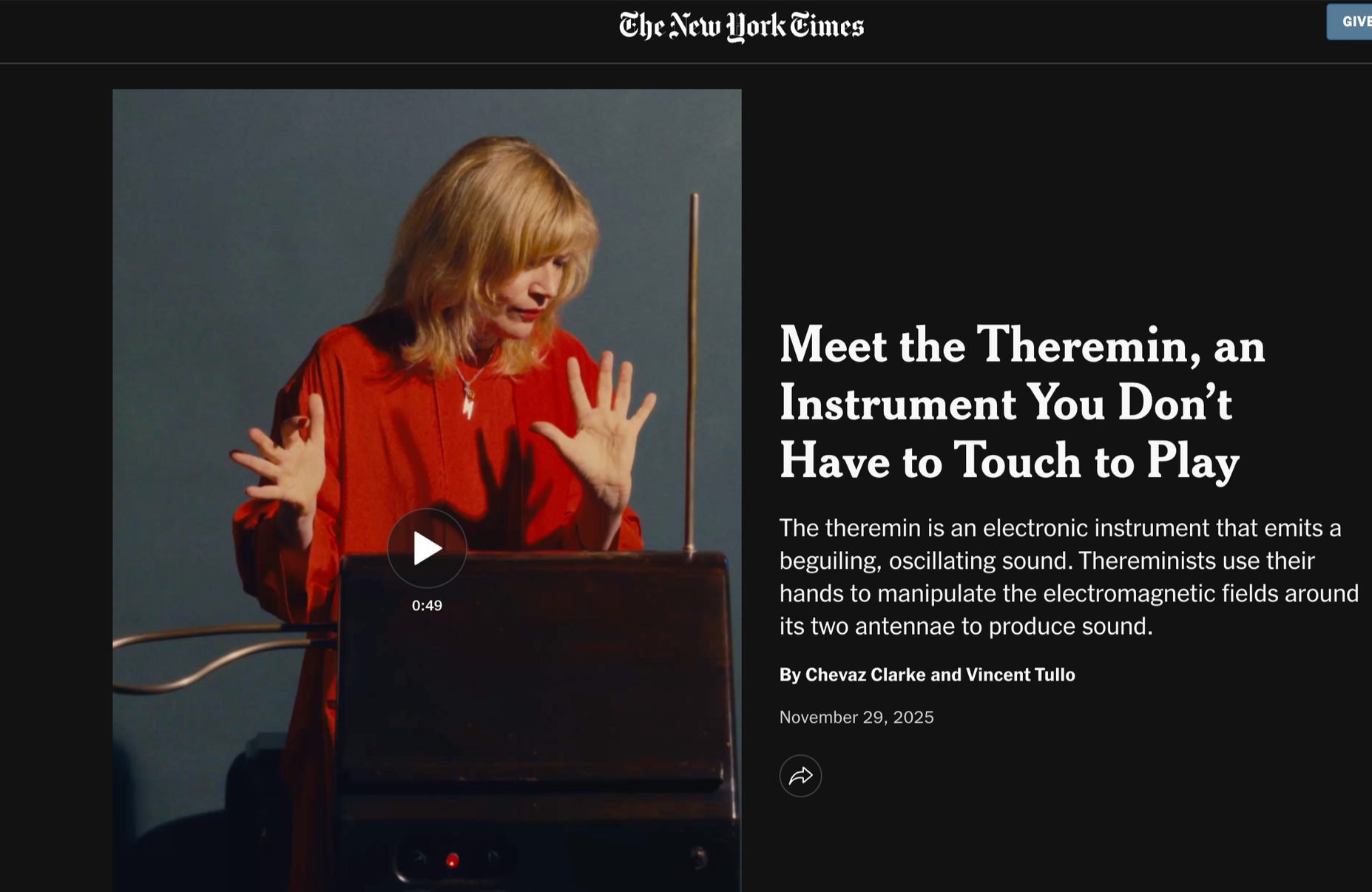 A woman with blonde hair dressed in a red top, with her hands raised, appears to be demonstrating or explaining a Theremin, an electronic musical instrument with antennas, on a dark background.