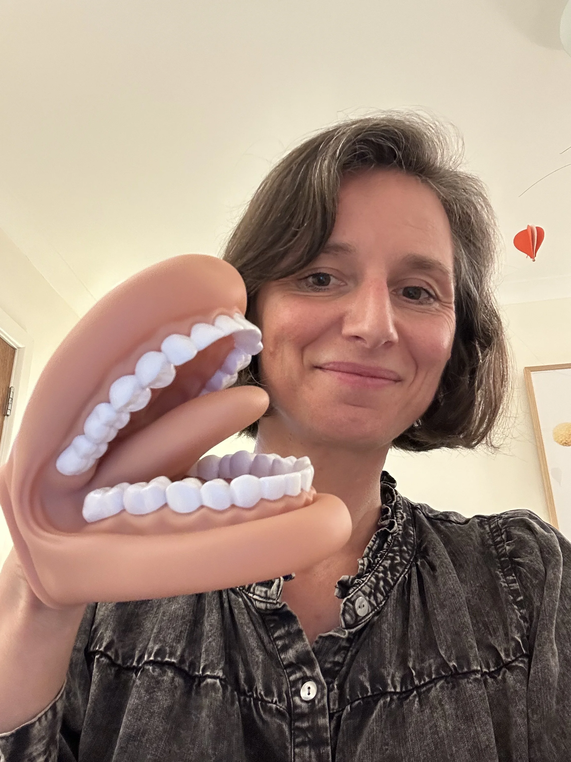 Woman holding up large set of fake teeth, smiling in an indoor setting.