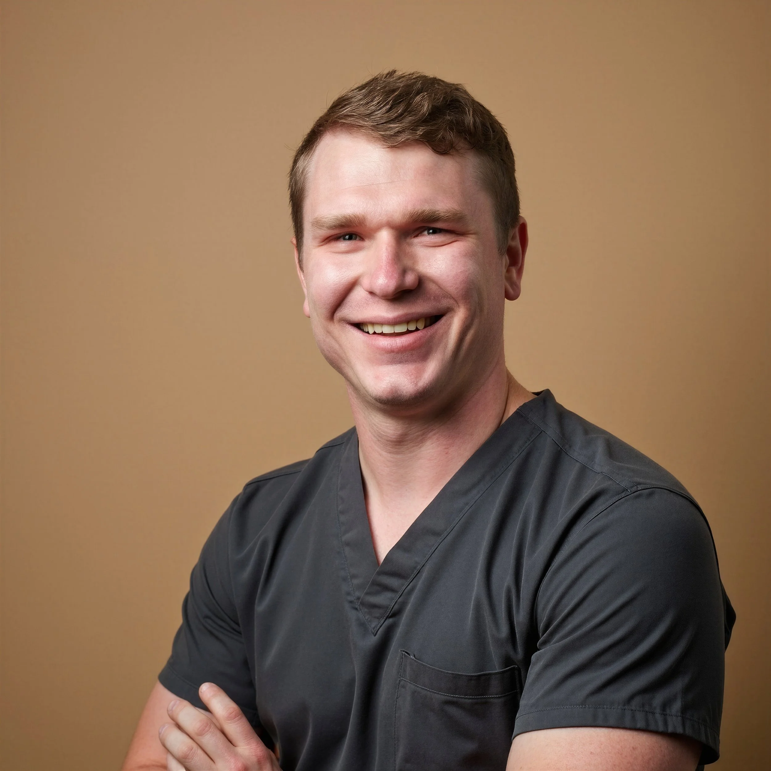 Headshot of a male healthcare professional, registered nurse Sean Halliday in gray scrubs smiling with arms crossed against a neutral background.