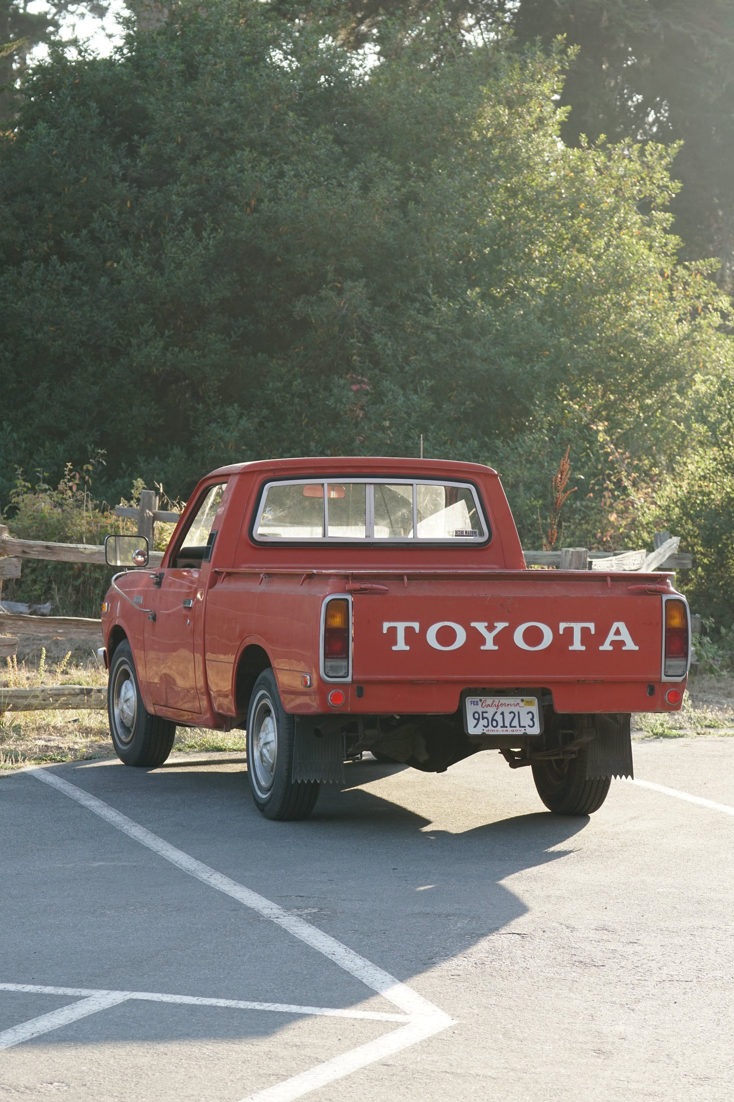 Red Toyota pickup truck parked in a lot with a background of trees and sunlight.
