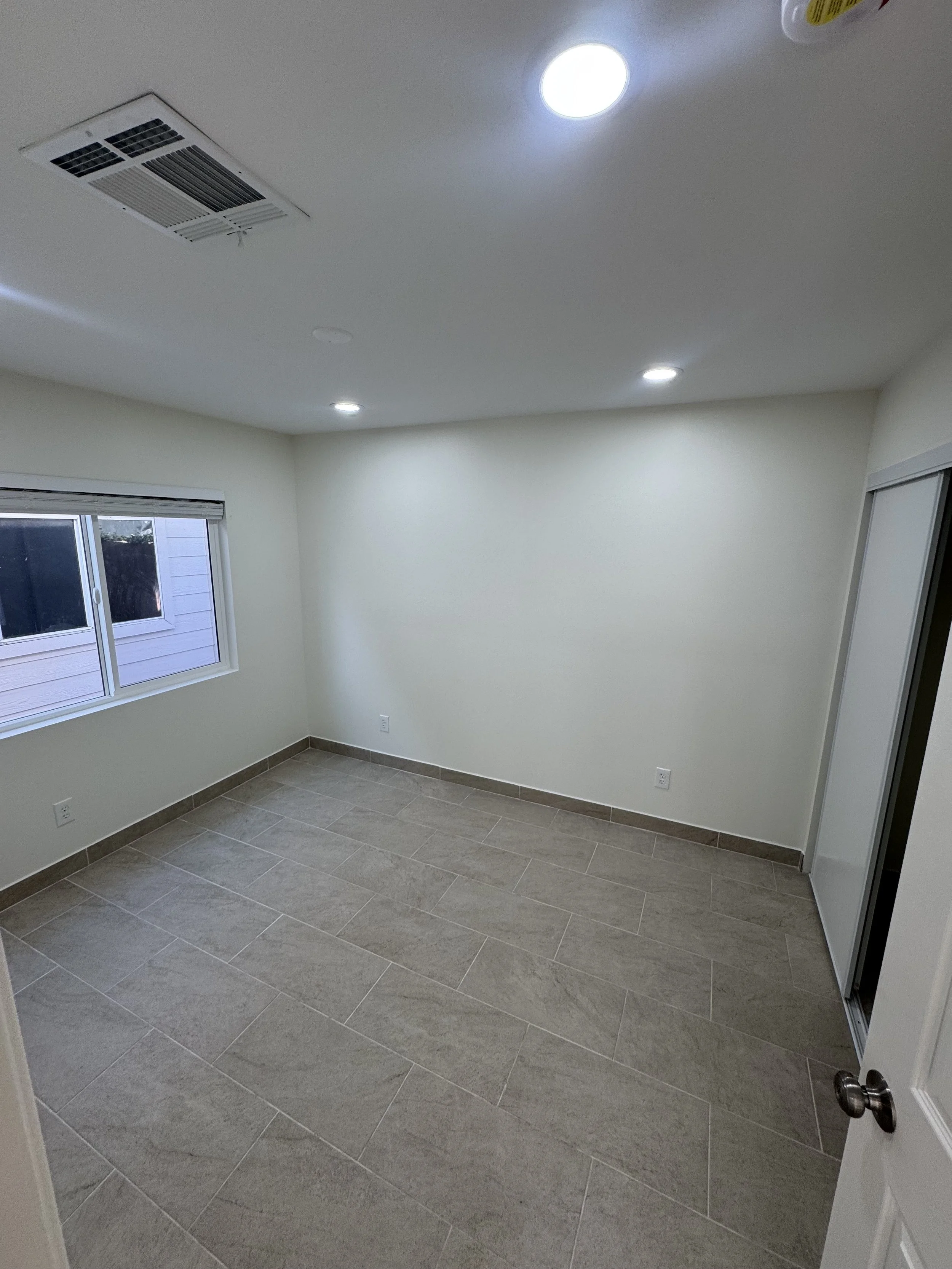 Empty room with beige tile flooring, white walls, a window with blinds, and a sliding door.