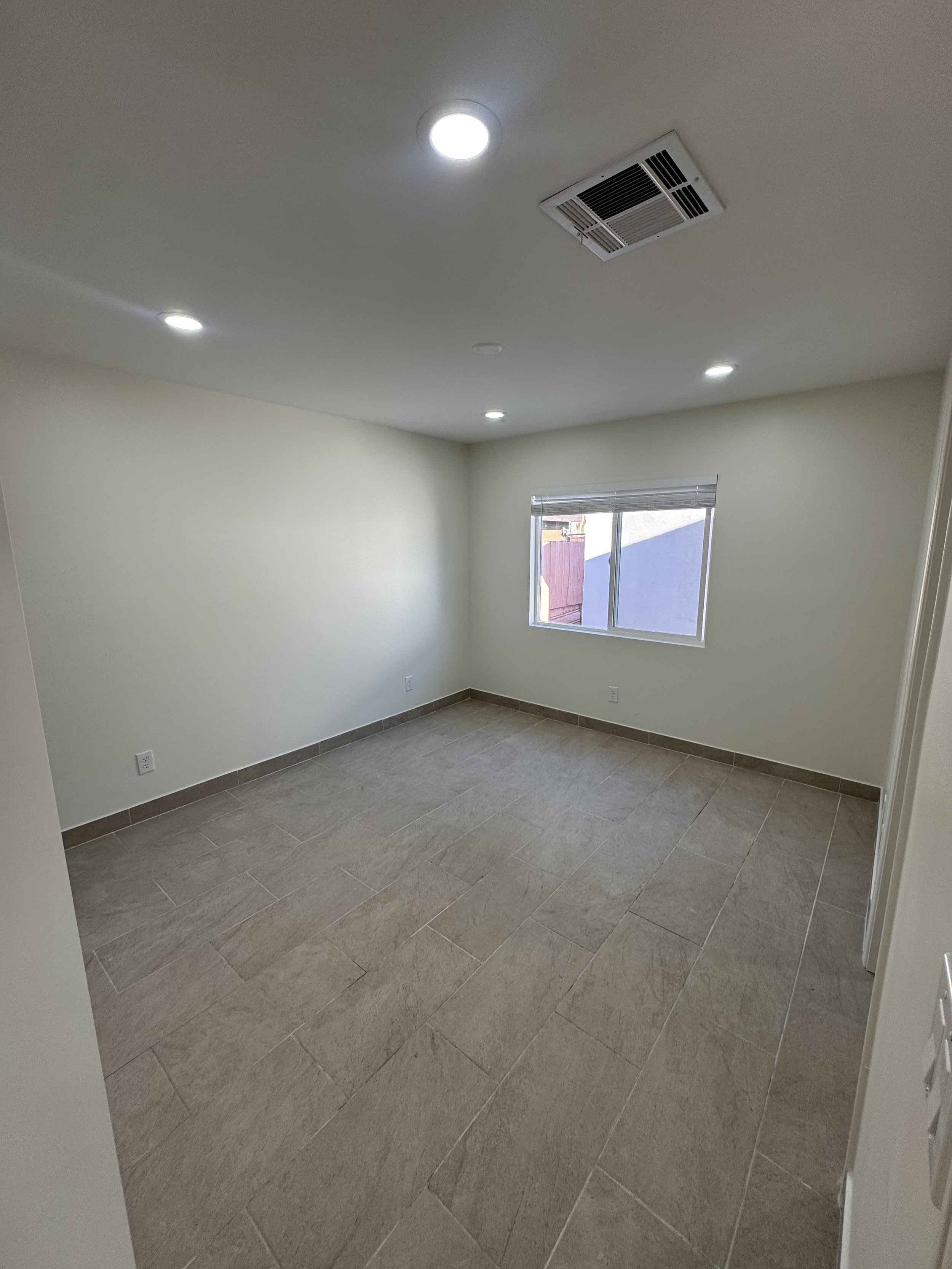 Empty room with beige tiled floor, white walls, a window, and ceiling lights.