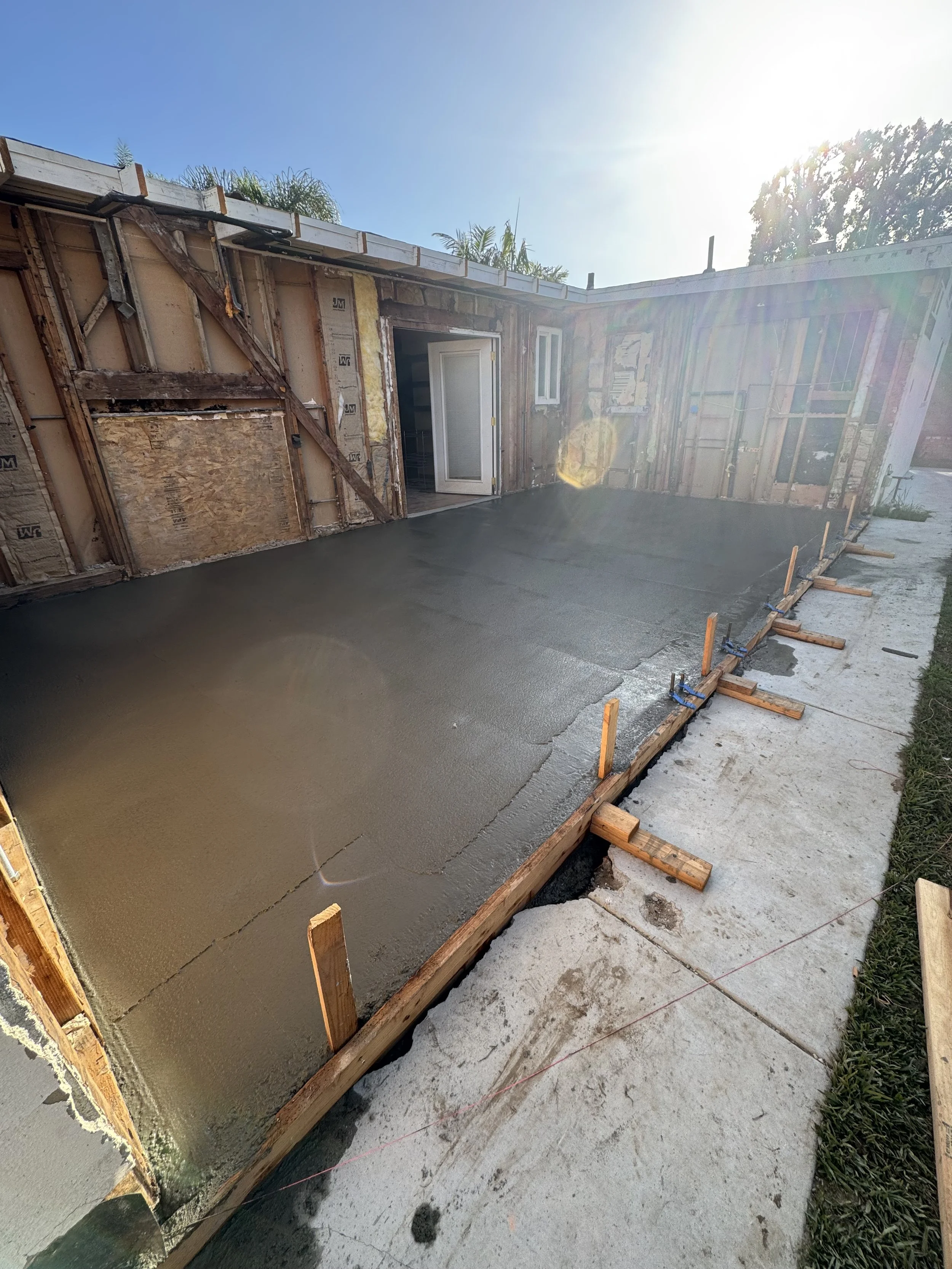 Concrete being poured for a new patio or walkway outside a house under construction, with sunlight shining in the background.