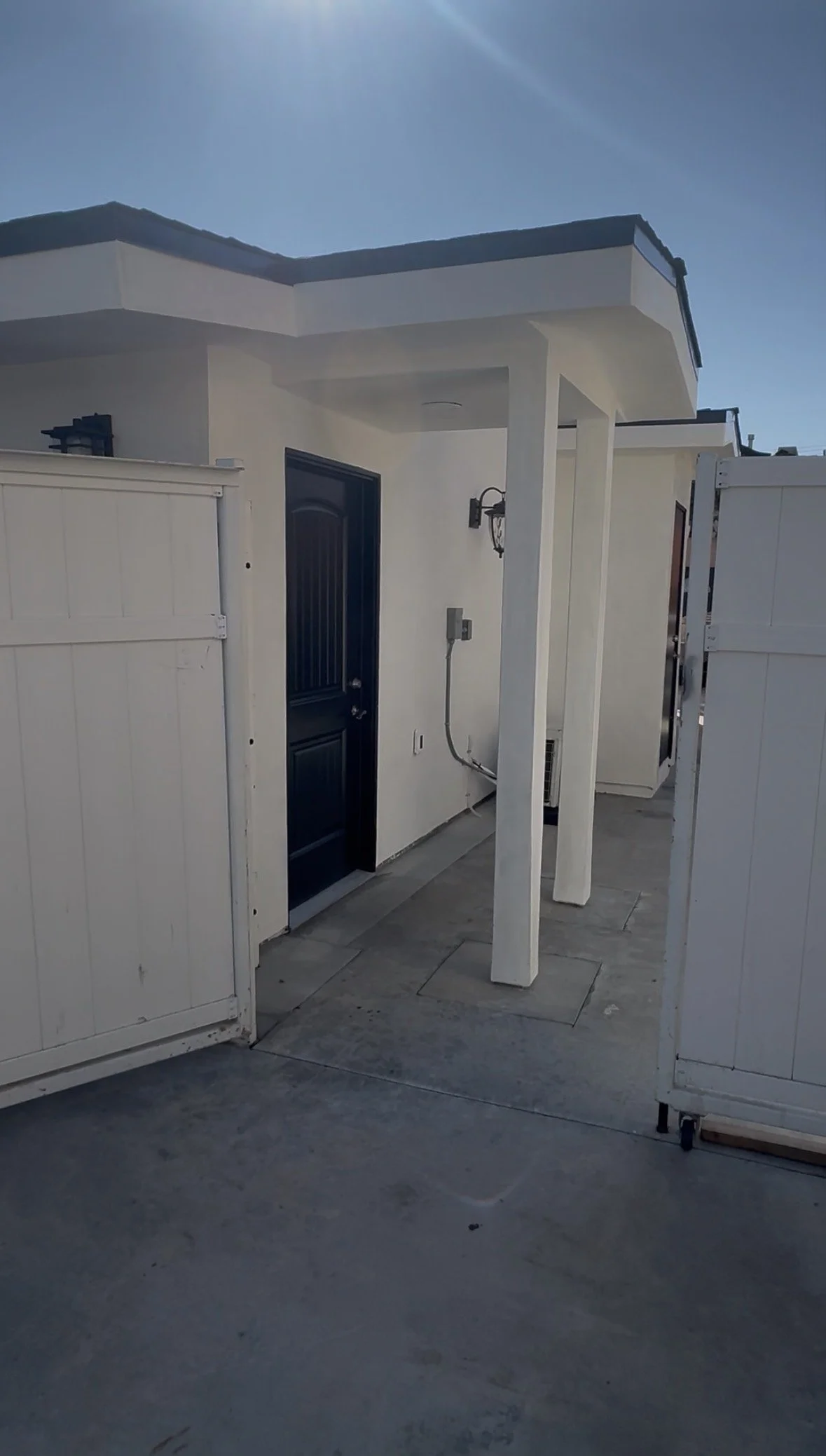 Outdoor area with a black door, white walls, a covered porch, and white fences on each side.