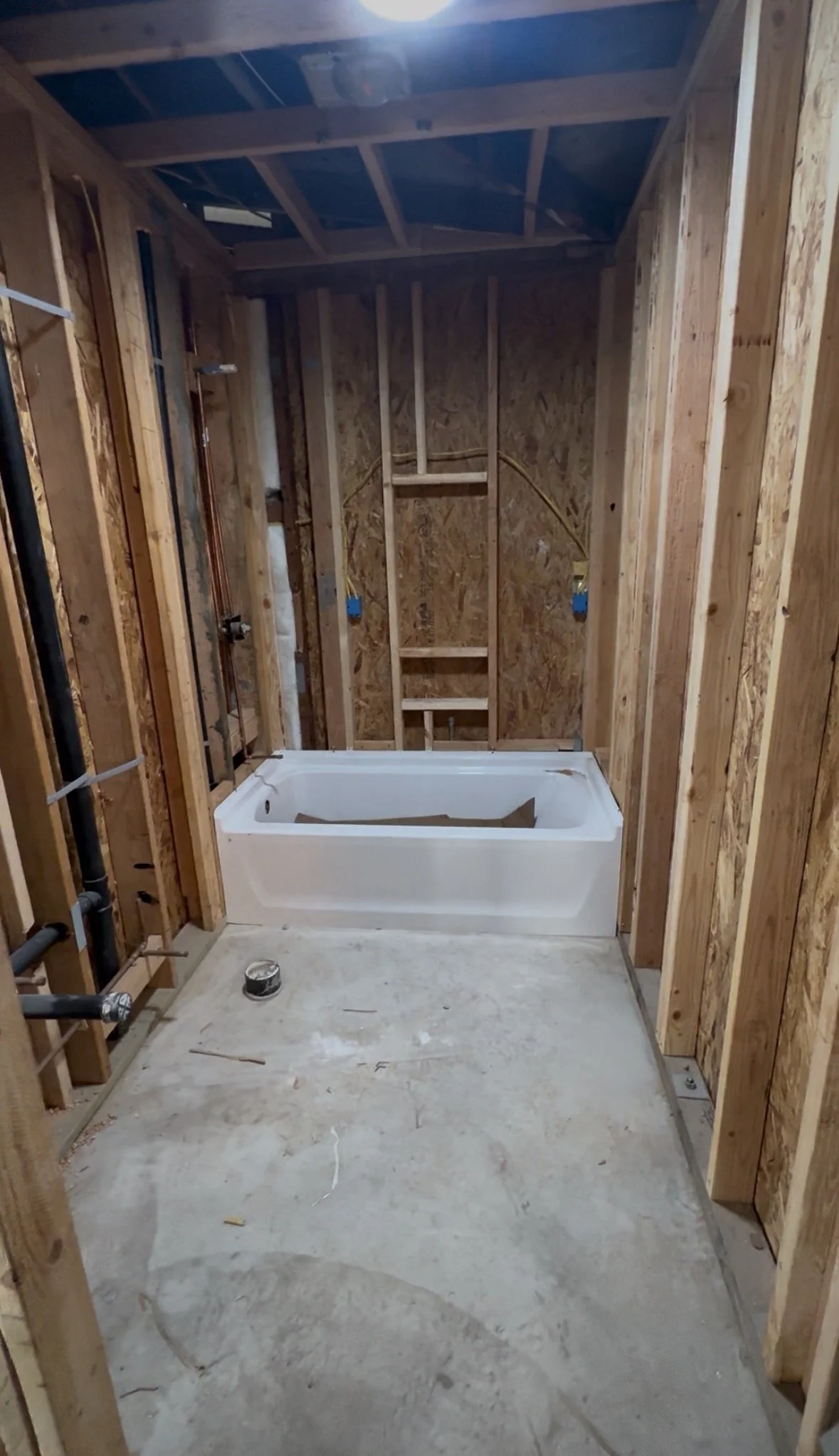 Under construction bathroom with wooden framing, an installed bathtub, and plumbing visible.