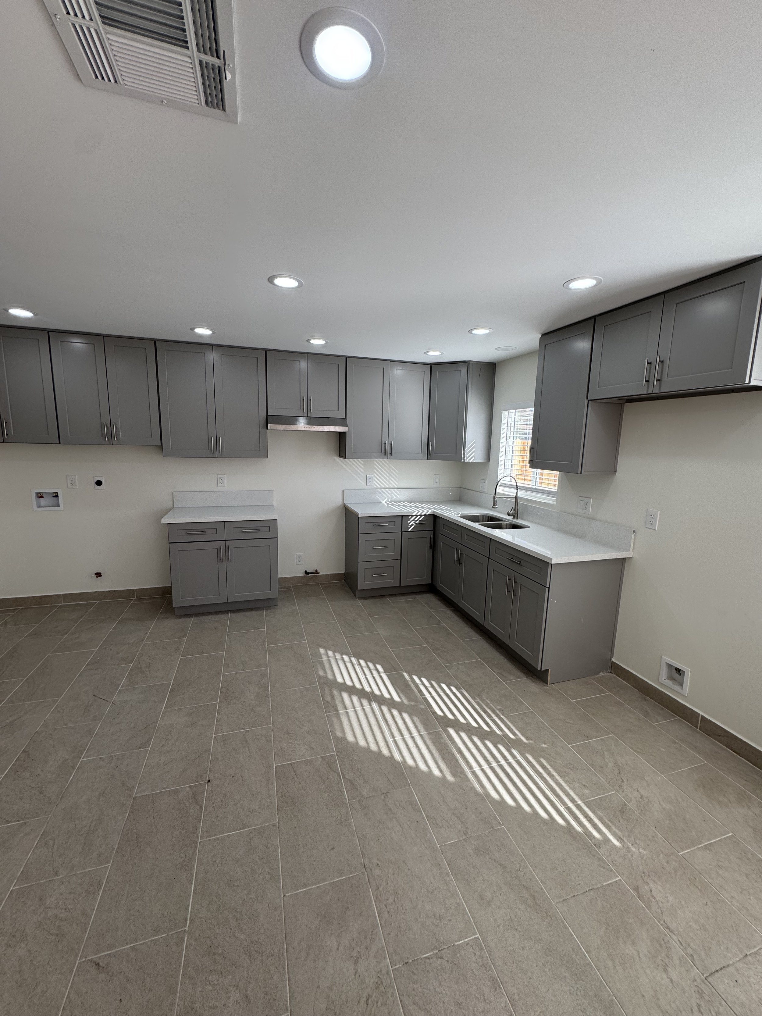 Empty kitchen with gray cabinets, white countertops, a window above the sink, tiled flooring, and ceiling lights.