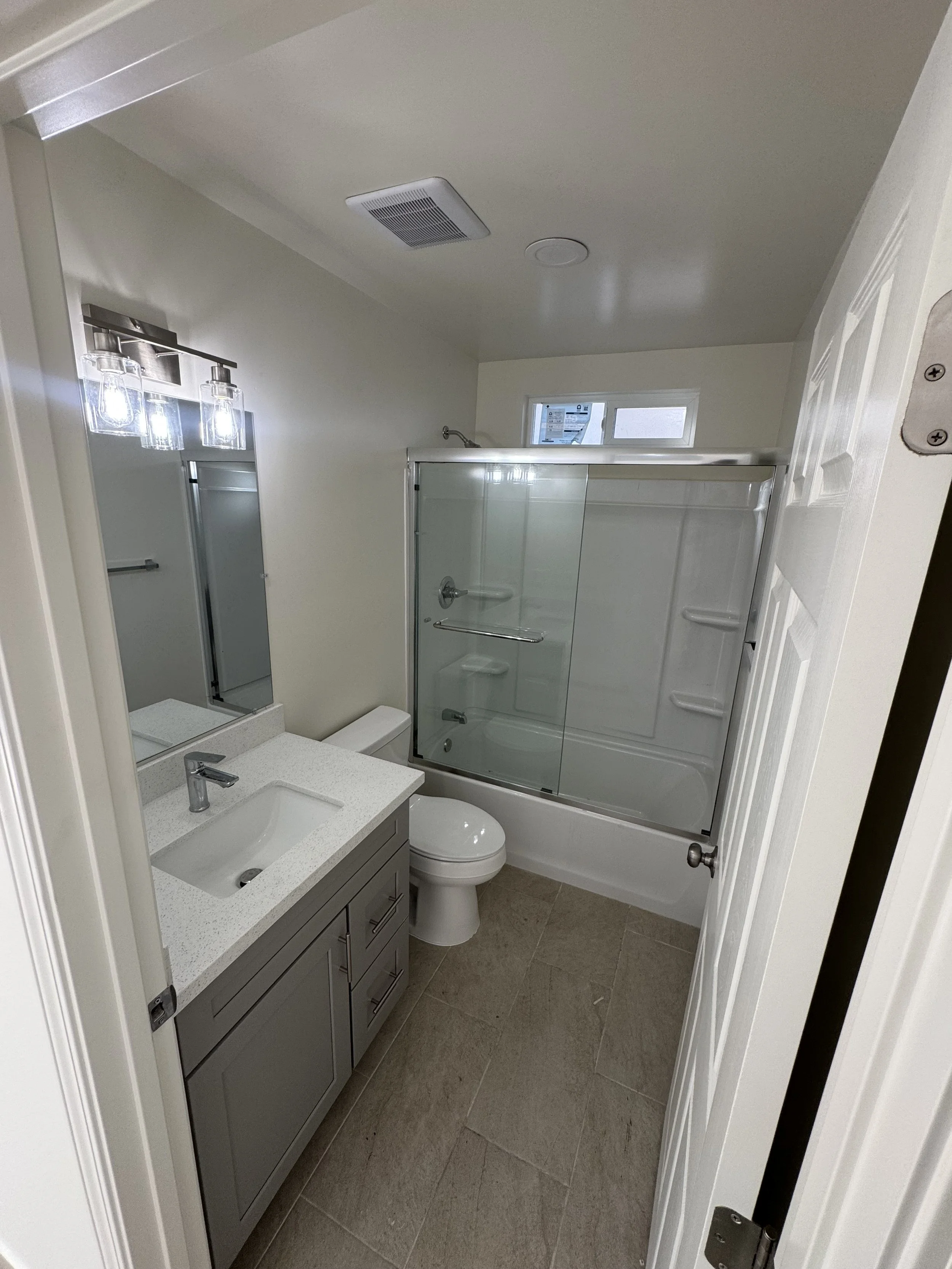 A small bathroom with a vanity sink, a toilet, and a bathtub with a glass door and a small window above it.