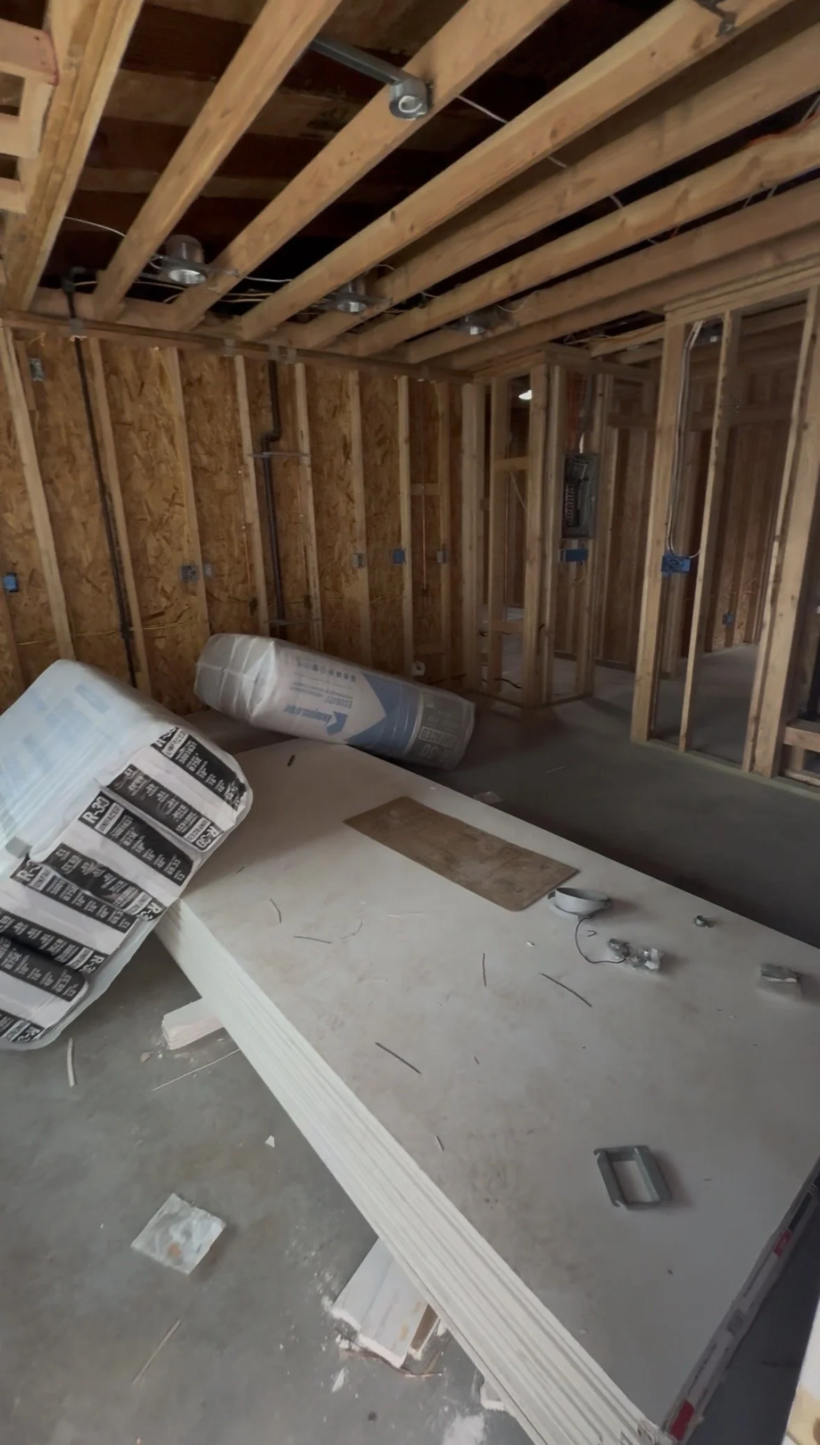 Interior of a house under construction with exposed wooden studs, wiring, and insulation materials.}