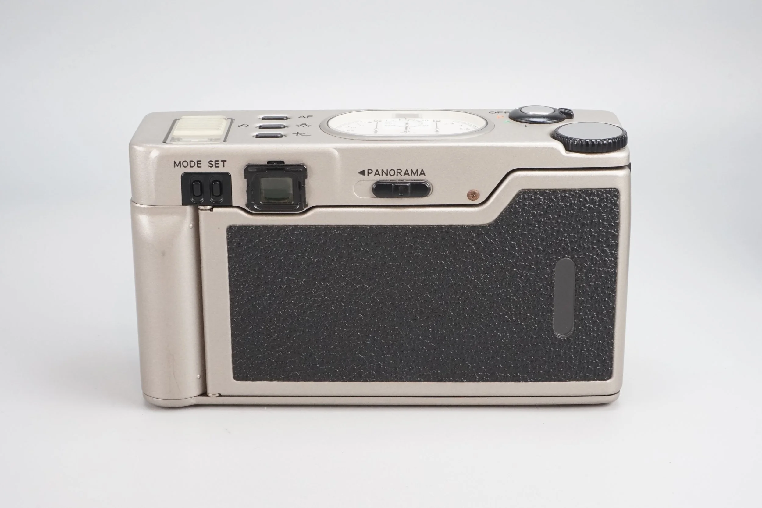 銀色のフィルムカメラ。背面にレンズ部分と操作ダイヤル、ズーム設定スイッチとシャッターボタンが見える。