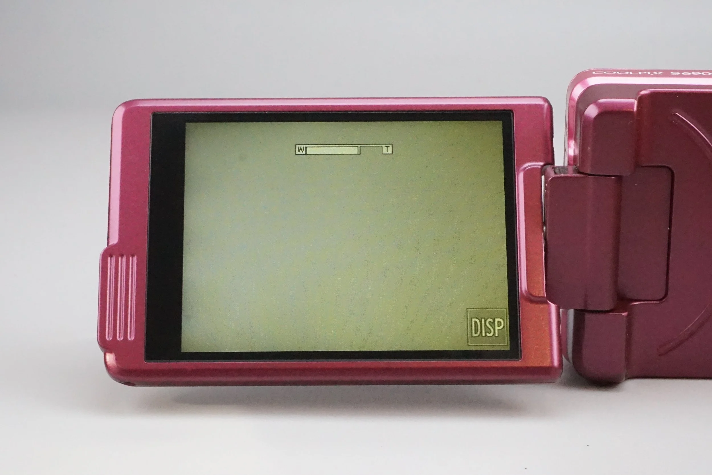 ピンク色のコンパクトデジタルカメラの液晶画面に、WとTの文字と矢印が表示されている。