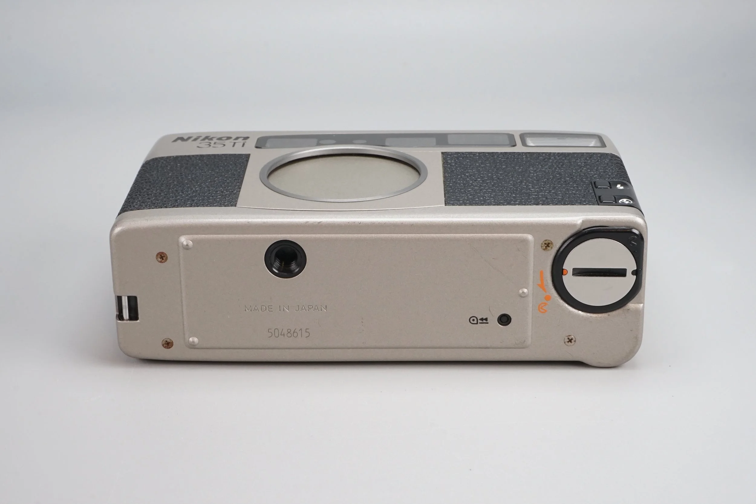 ニコンの古いカメラの底面の写真，底面には製造国やシリアル番号が記載されている、黒いダイヤルや小さな筺体が付いている。