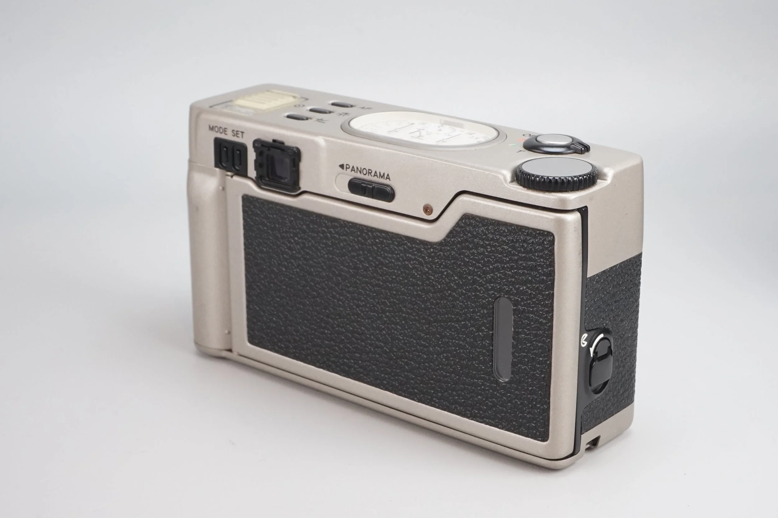 銀色のカメラ。背面と上部の操作パーツが写っている。