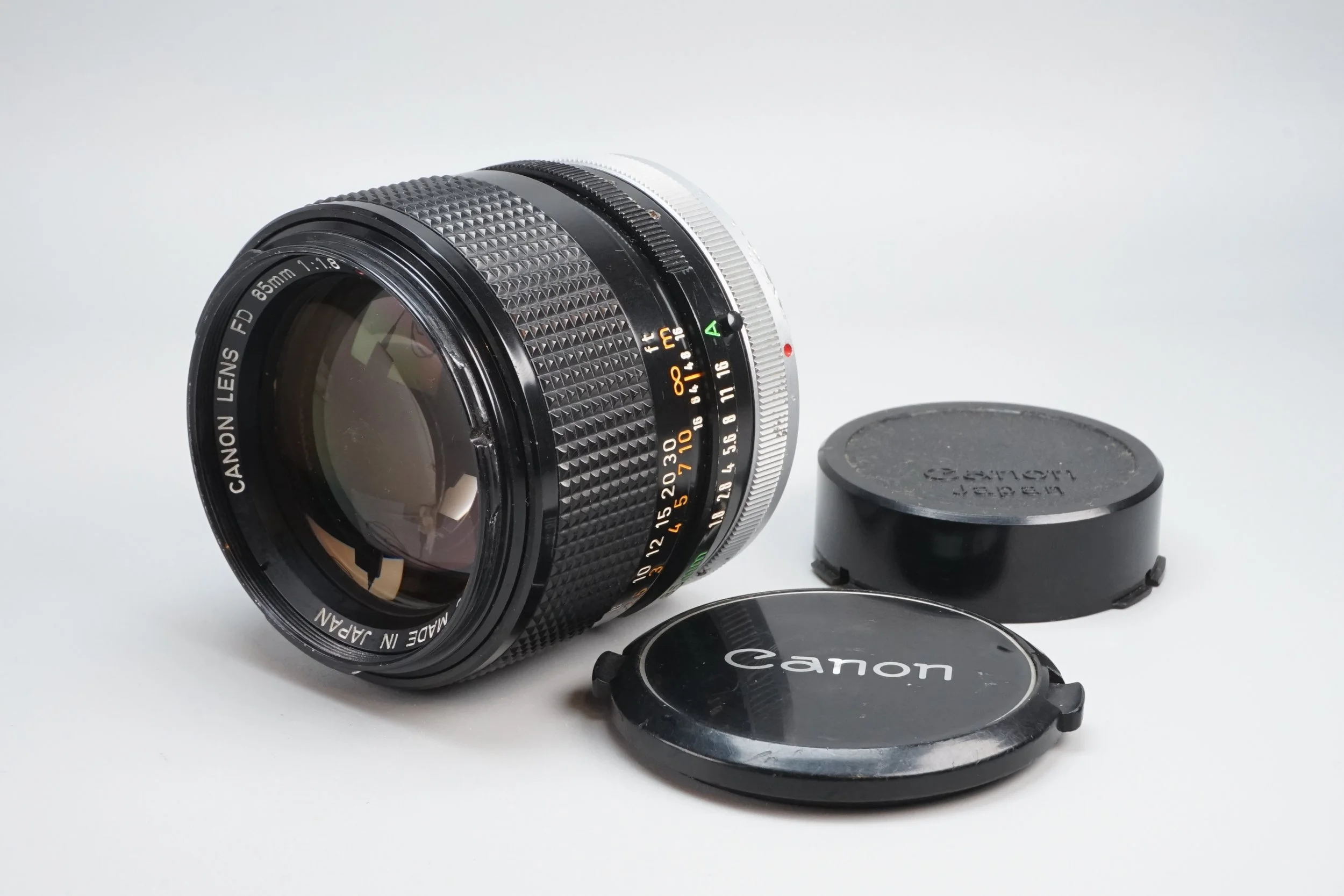 Canonの85mm F1.8カメラレンズとレンズキャップ、レンズフードが置かれている写真