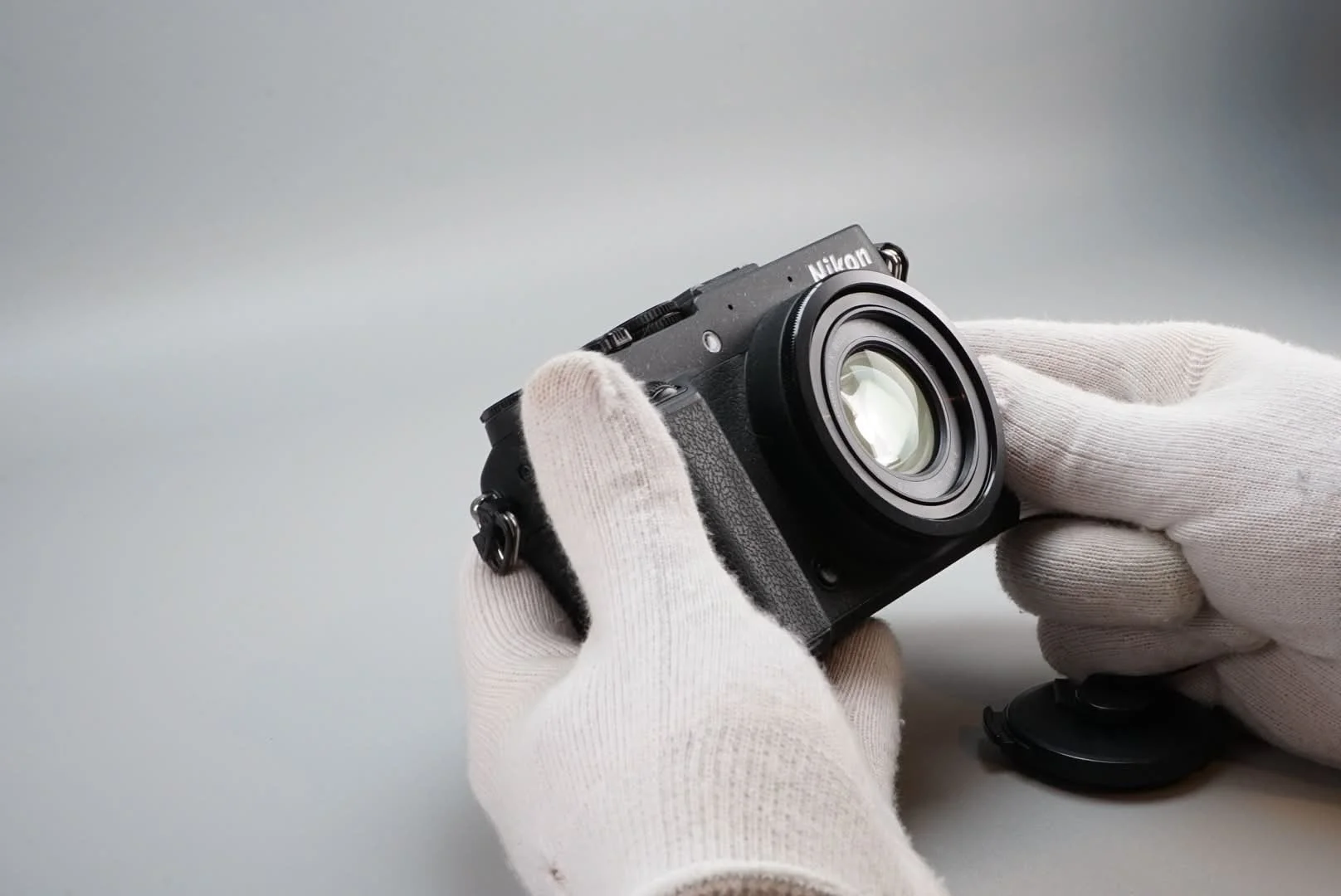 白い手袋をした人がニコンのデジタルカメラのレンズ部分を持っている写真