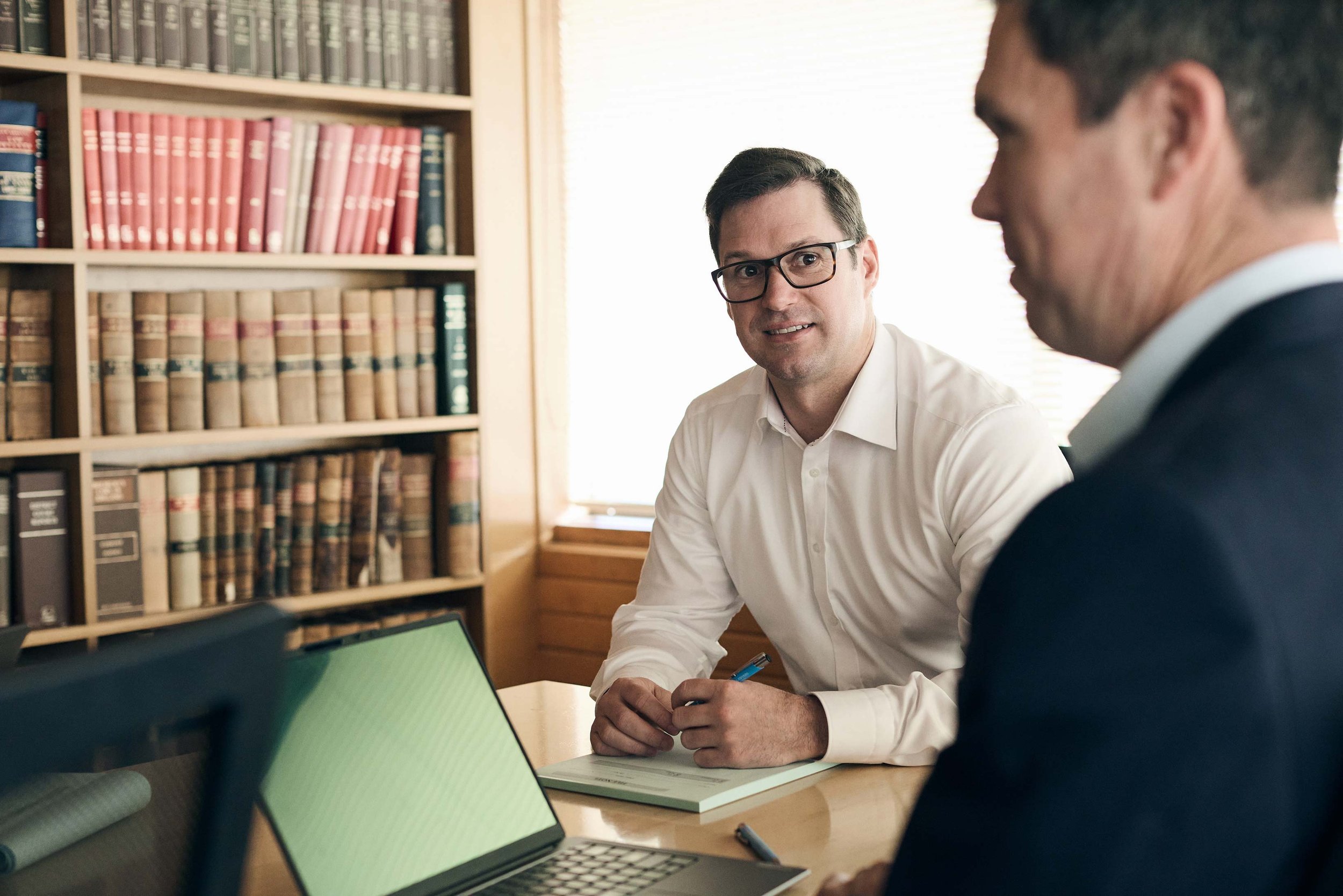Two men engaged in a conversation in a professional setting, with a bookshelf filled with legal books in the background.