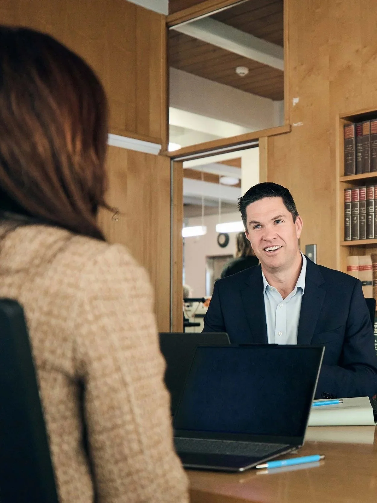 A man in a suit talking to a woman in a tan blazer in an office.