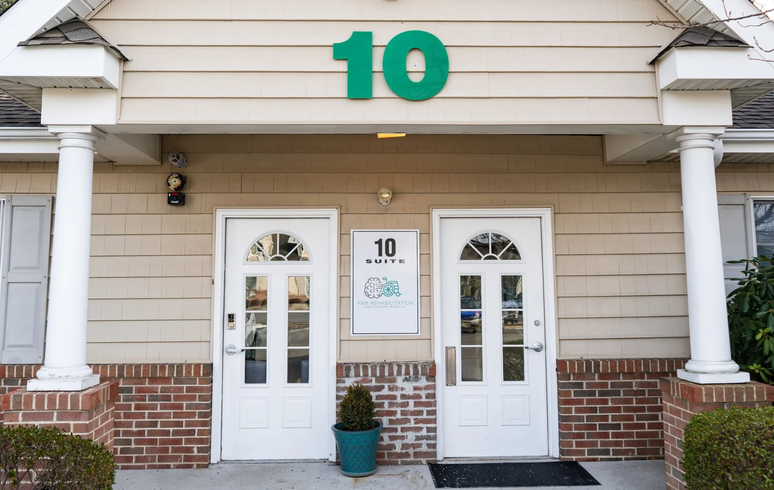 Building entrance with two white doors, a sign with house icon and text for fam rehabilitation, and a large teal number 10 above the entrance.