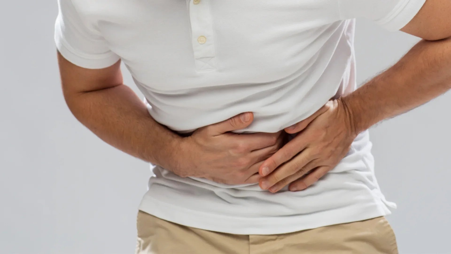 Person clutching stomach in pain, wearing a white shirt and beige pants.