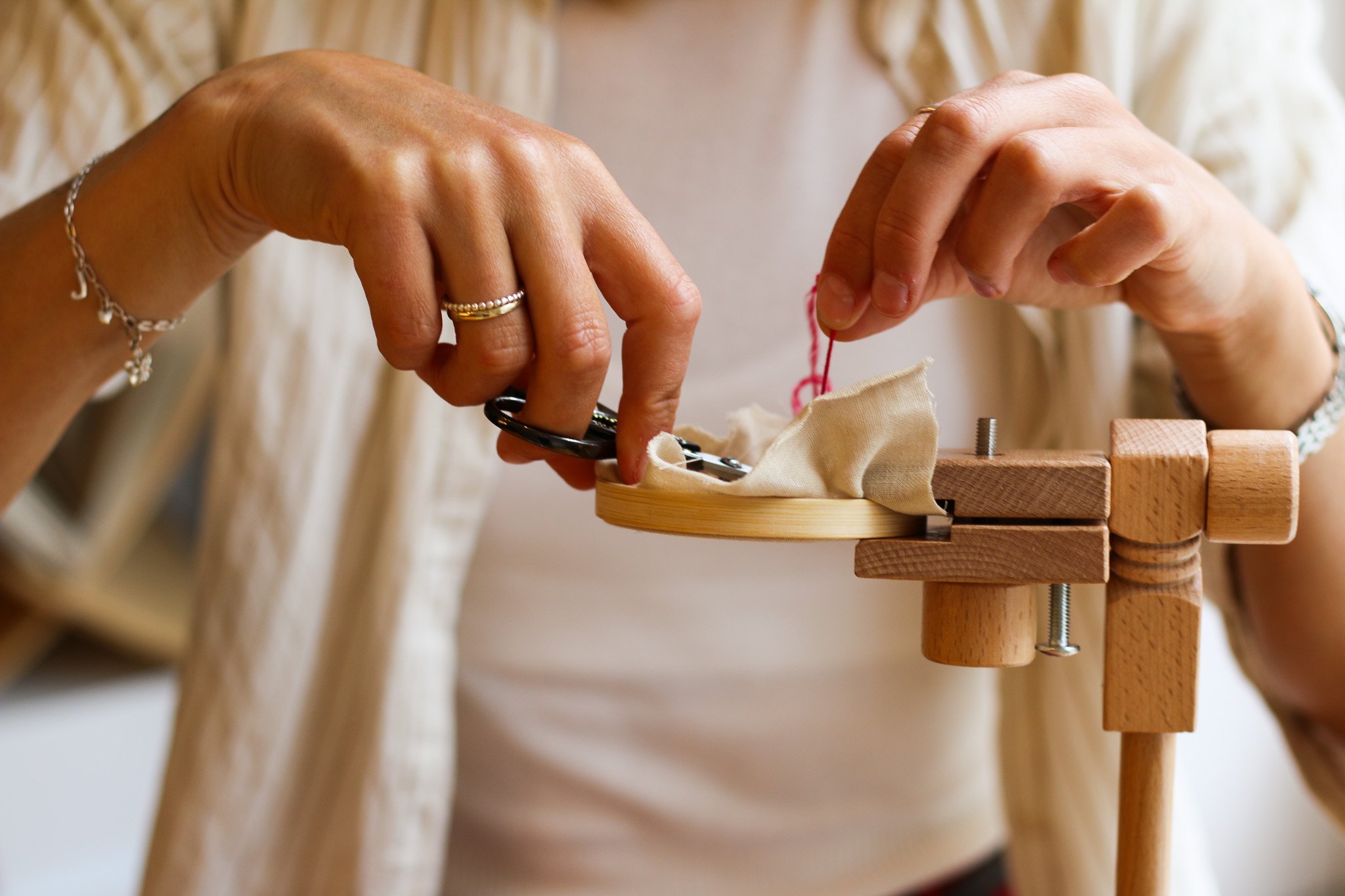 A person sewing fabric on a wooden-based embroidery hoop clamped to a wooden sewing press, with their hands visible guiding the fabric.