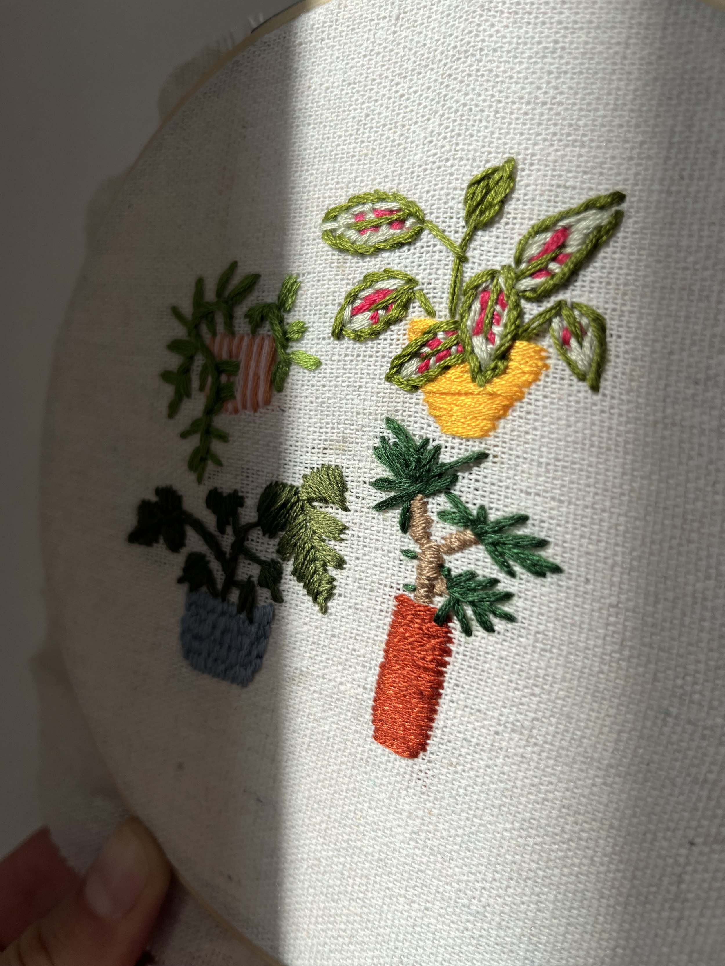 Embroidery of a potted plant, a watering can, and a carrot on fabric.