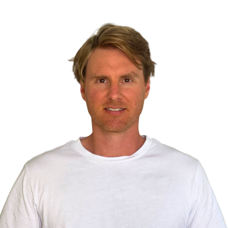 A man with light brown hair and a white T-shirt smiling at the camera against a plain white background.