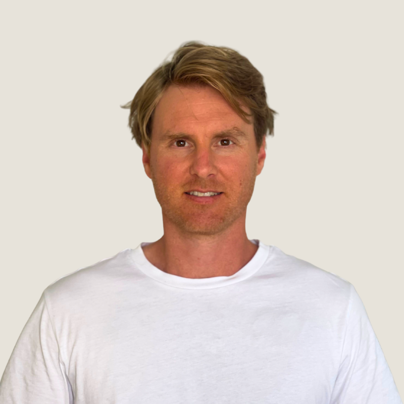 A young man with light brown hair wearing a white t-shirt, standing against a plain light background.