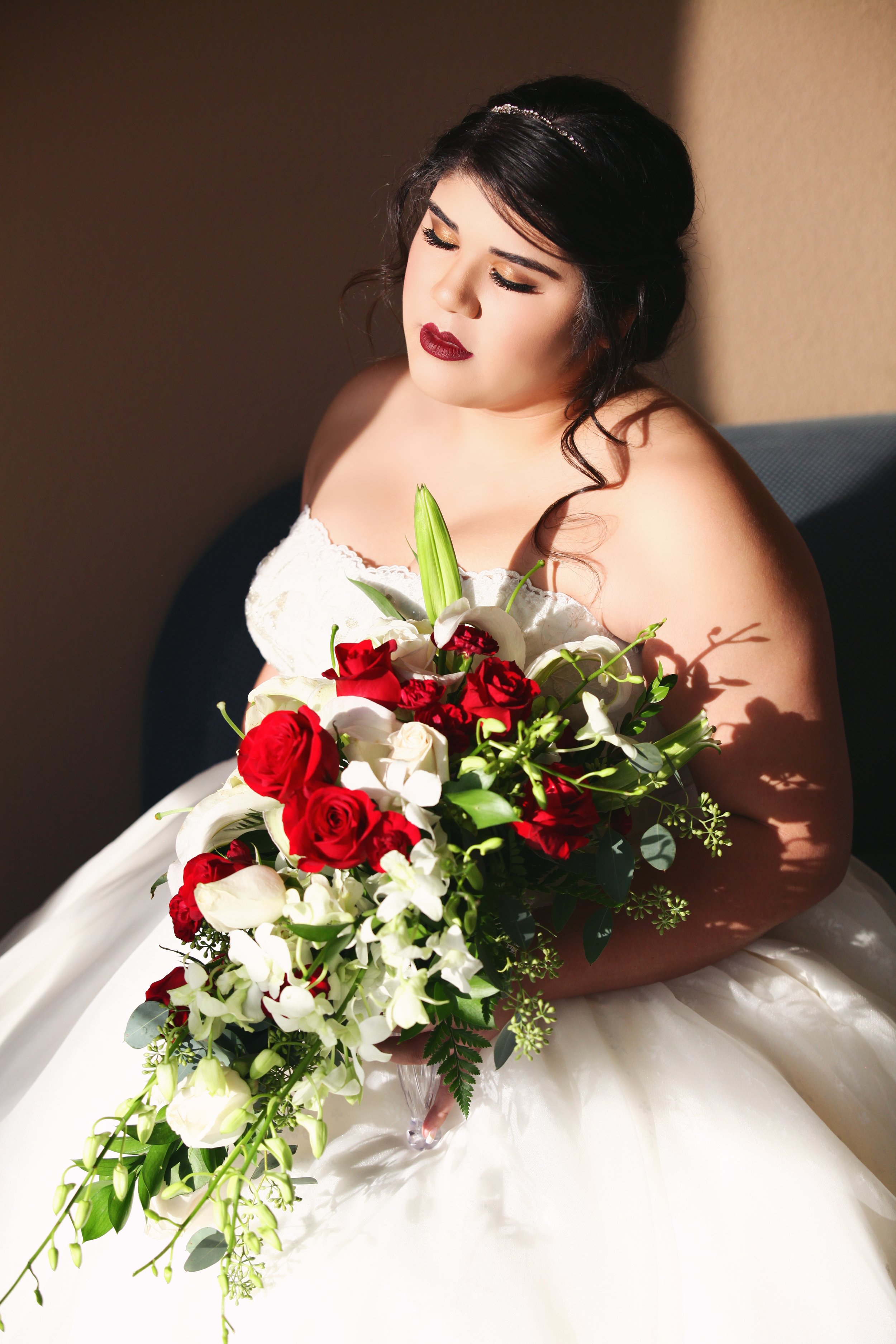 A woman in a wedding dress holding a large bouquet of red and white flowers.
