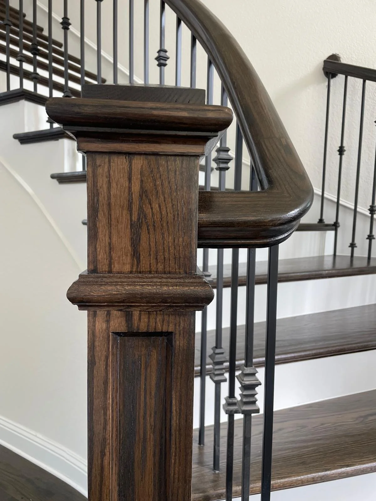 Close-up of a wooden staircase newel post with dark wood finish and black metal balusters in a modern home interior.