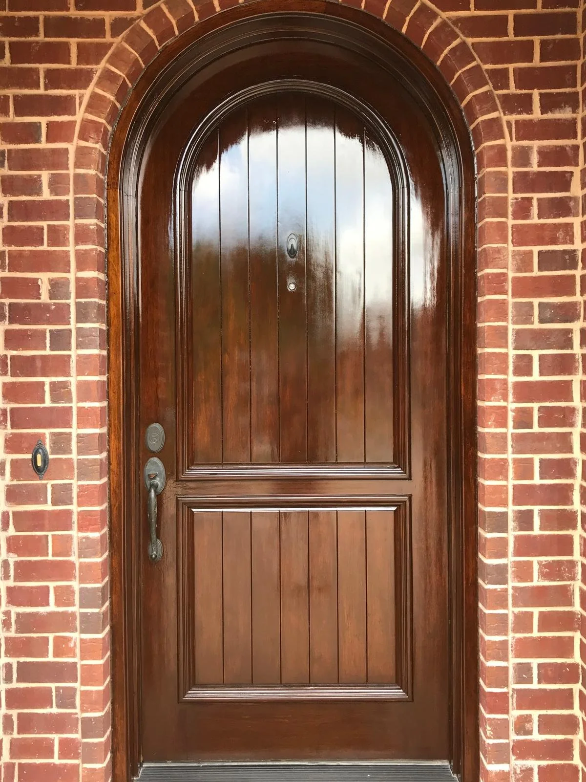 A wooden front door with an arched top, surrounded by a brick wall.