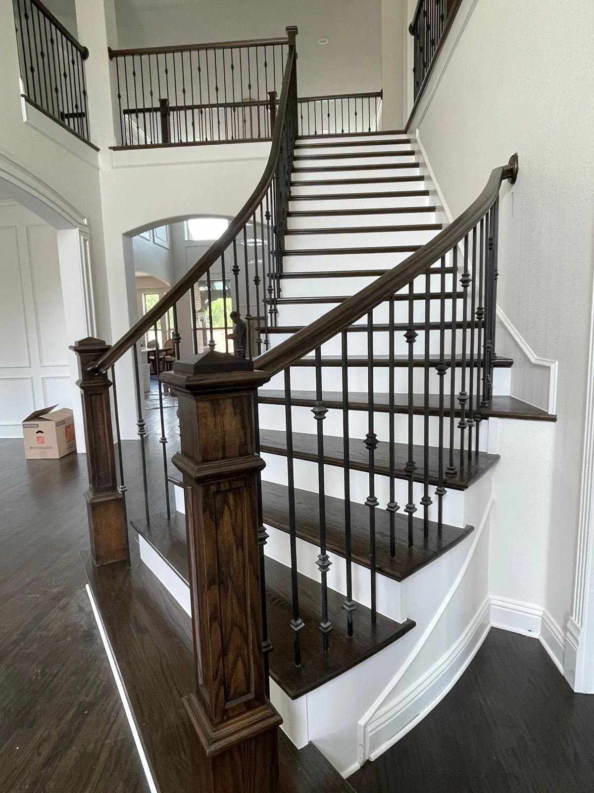 A staircase with dark wood flooring and dark wood handrails leading up to a second level, with black metal balusters and white walls inside a modern home.