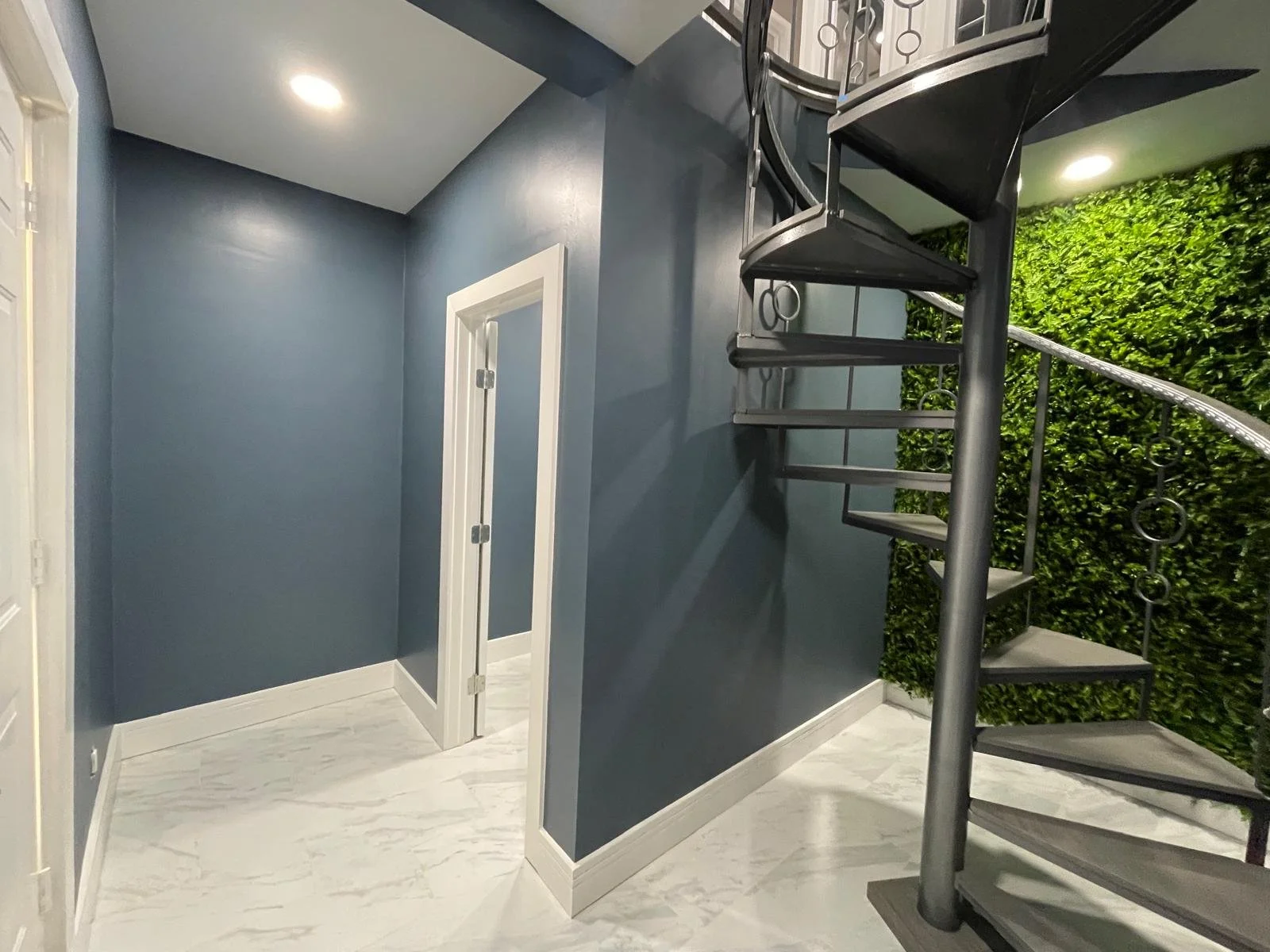 Interior view of a modern staircase next to a green wall, with blue painted walls, white trim, and marble-patterned flooring.