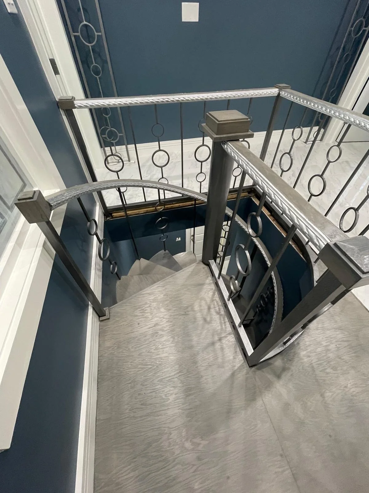 View of a spiral staircase with metal railing and wooden steps, seen from above, inside a house with dark blue walls and white trim.