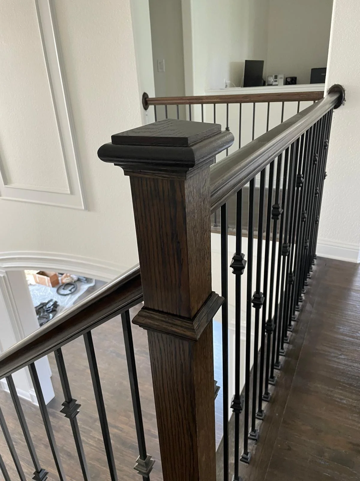 Close-up of a staircase railing with a wooden newel post and black metal balusters in a home interior.