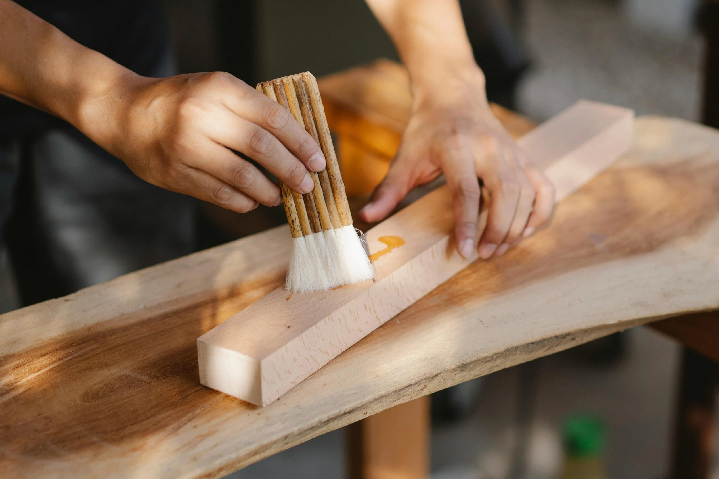 Person applying stain or finish to a piece of wood using a brush.