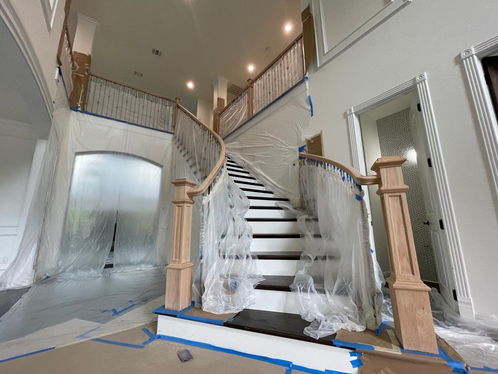 Interior of a house staircase during renovation, with protective plastic sheeting and tape covering parts of the staircase and railing.