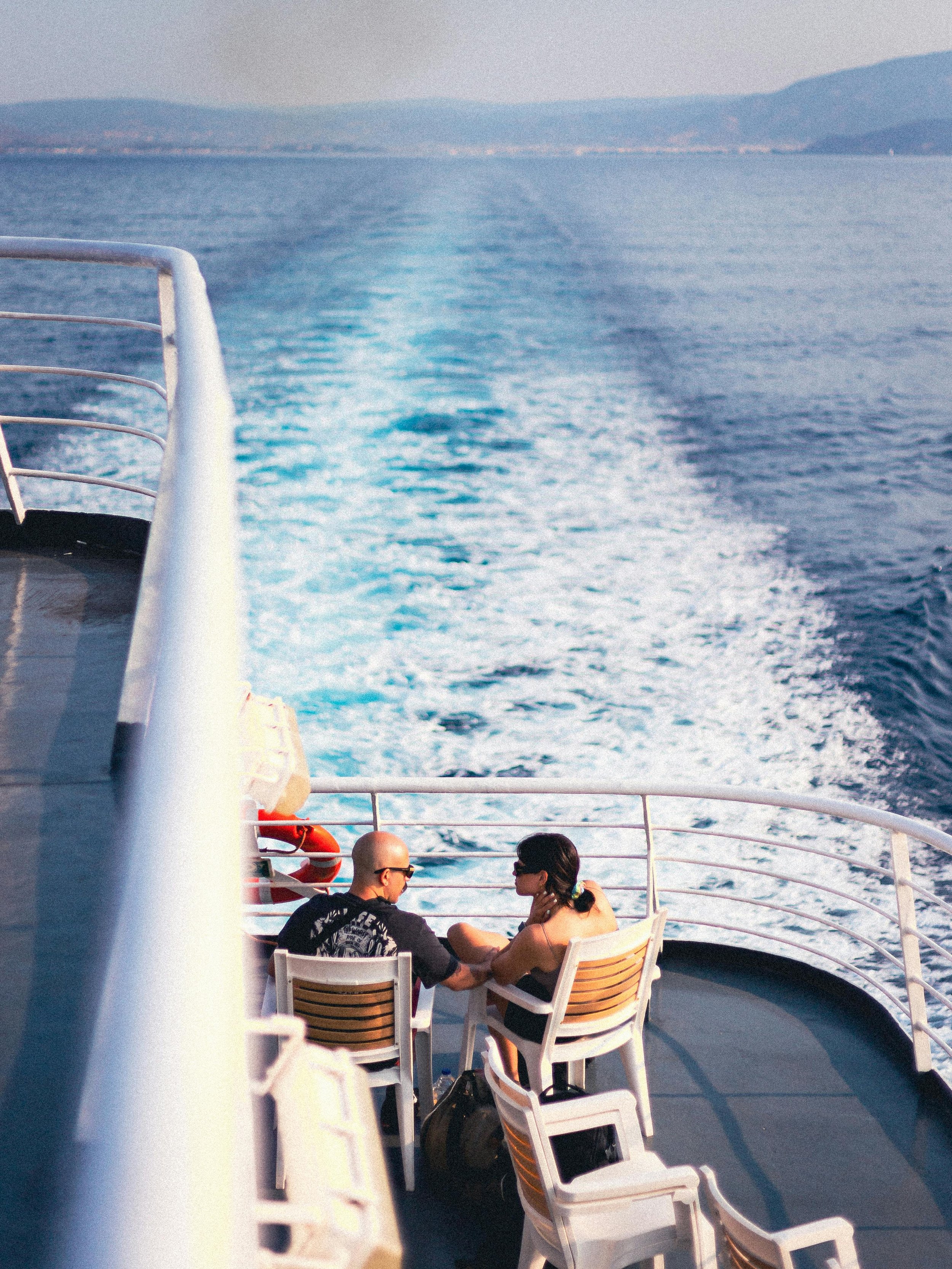 Two people sitting and talking on a boat deck with water and horizon in the background.