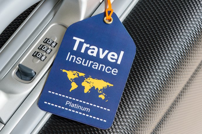Blue travel insurance tag with yellow world map graphic hanging inside an airplane, attached to a black textured surface, with a combination lock in the background.