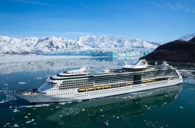 Large cruise ship sailing in icy waters with snow-covered mountains in the background.