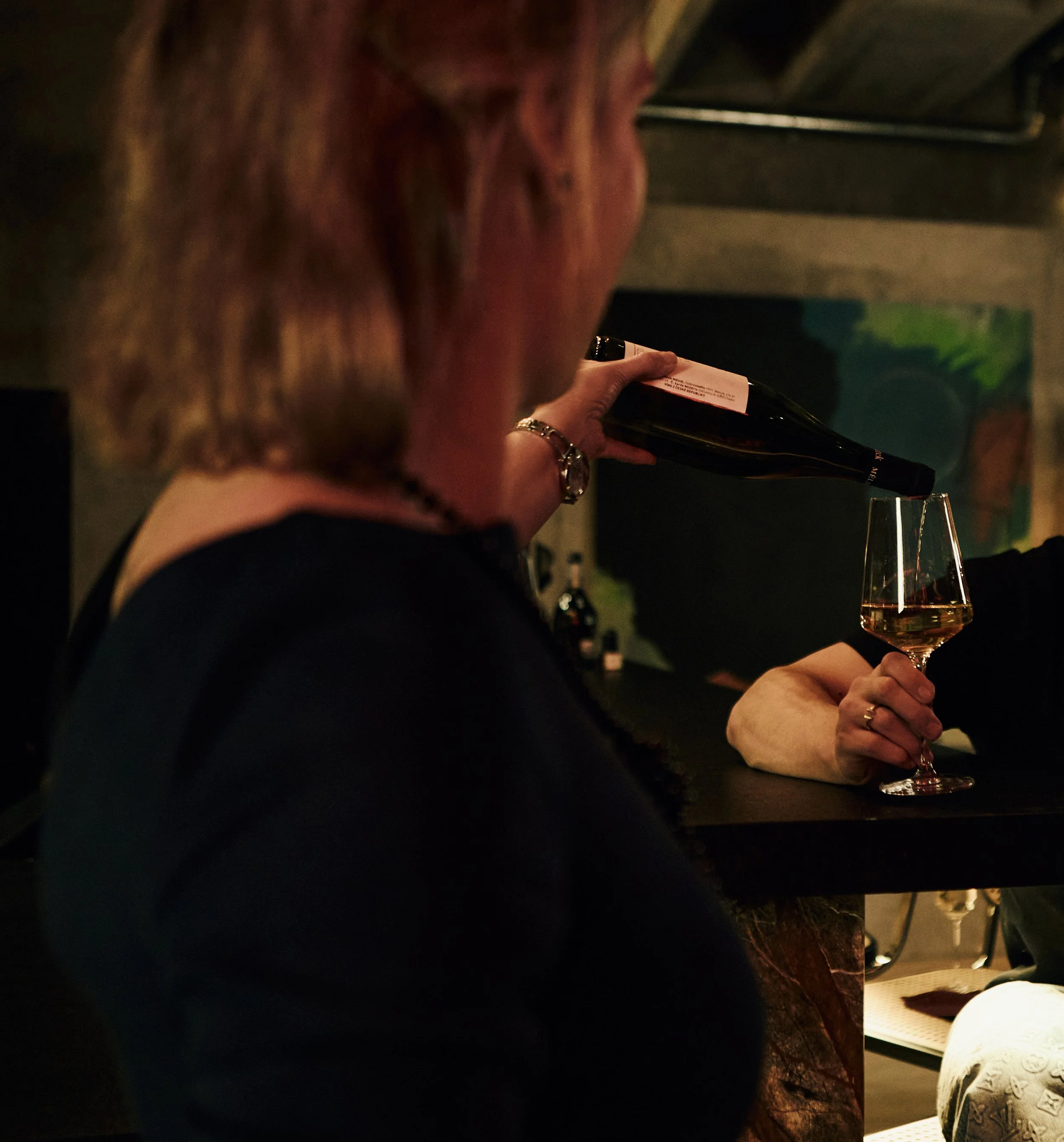 Person pouring wine into a glass at a dimly lit bar or wine tasting event.