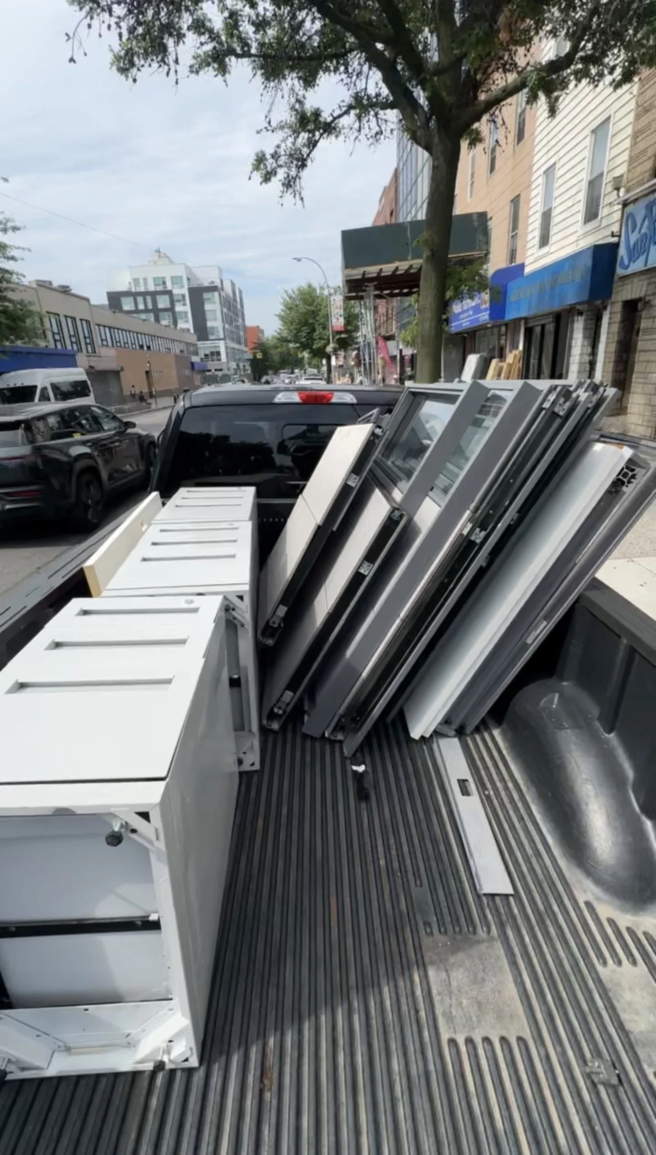 A flatbed truck parked on city street loaded with white metal cabinets, possibly on their way to a business or construction site.