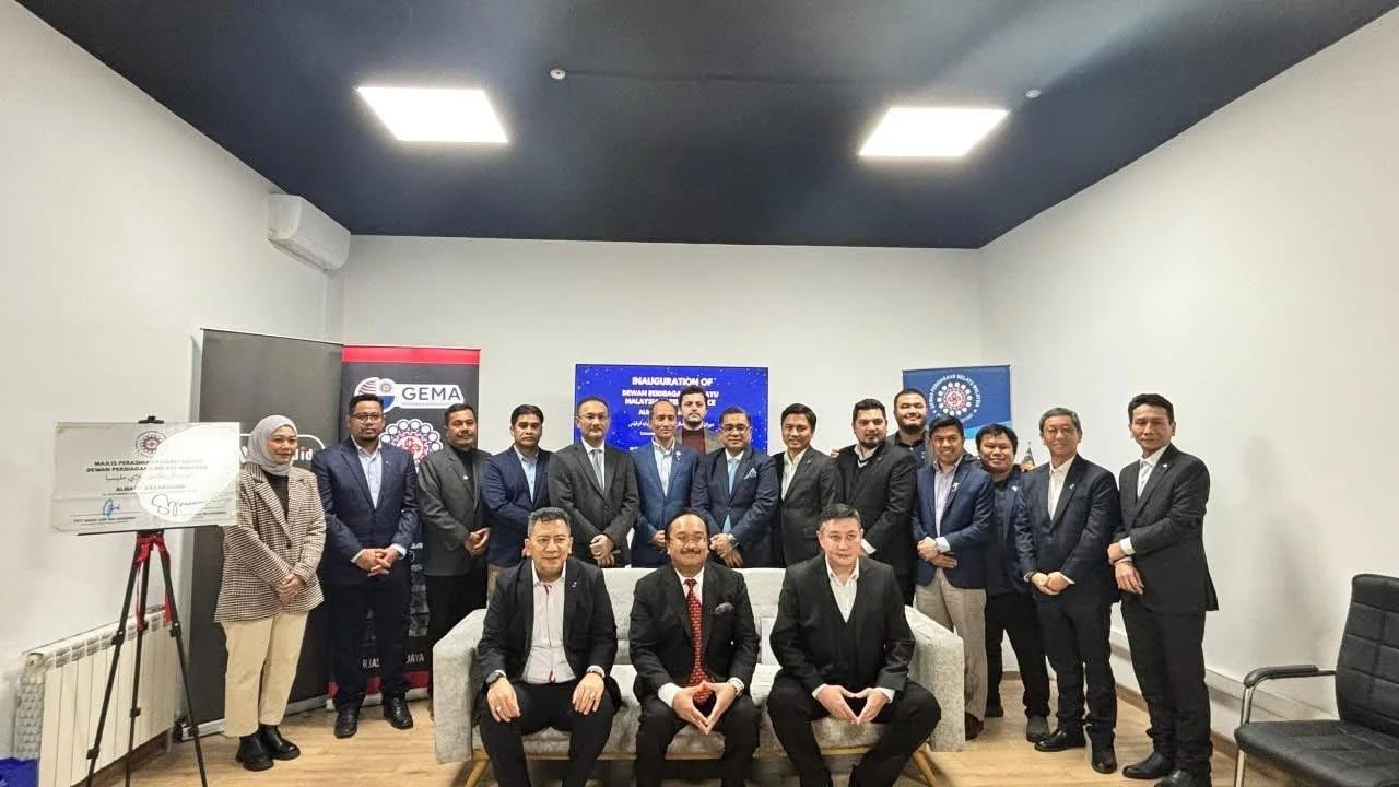 Group of professionals in formal attire at an indoor event, with banners and a presentation screen in the background.